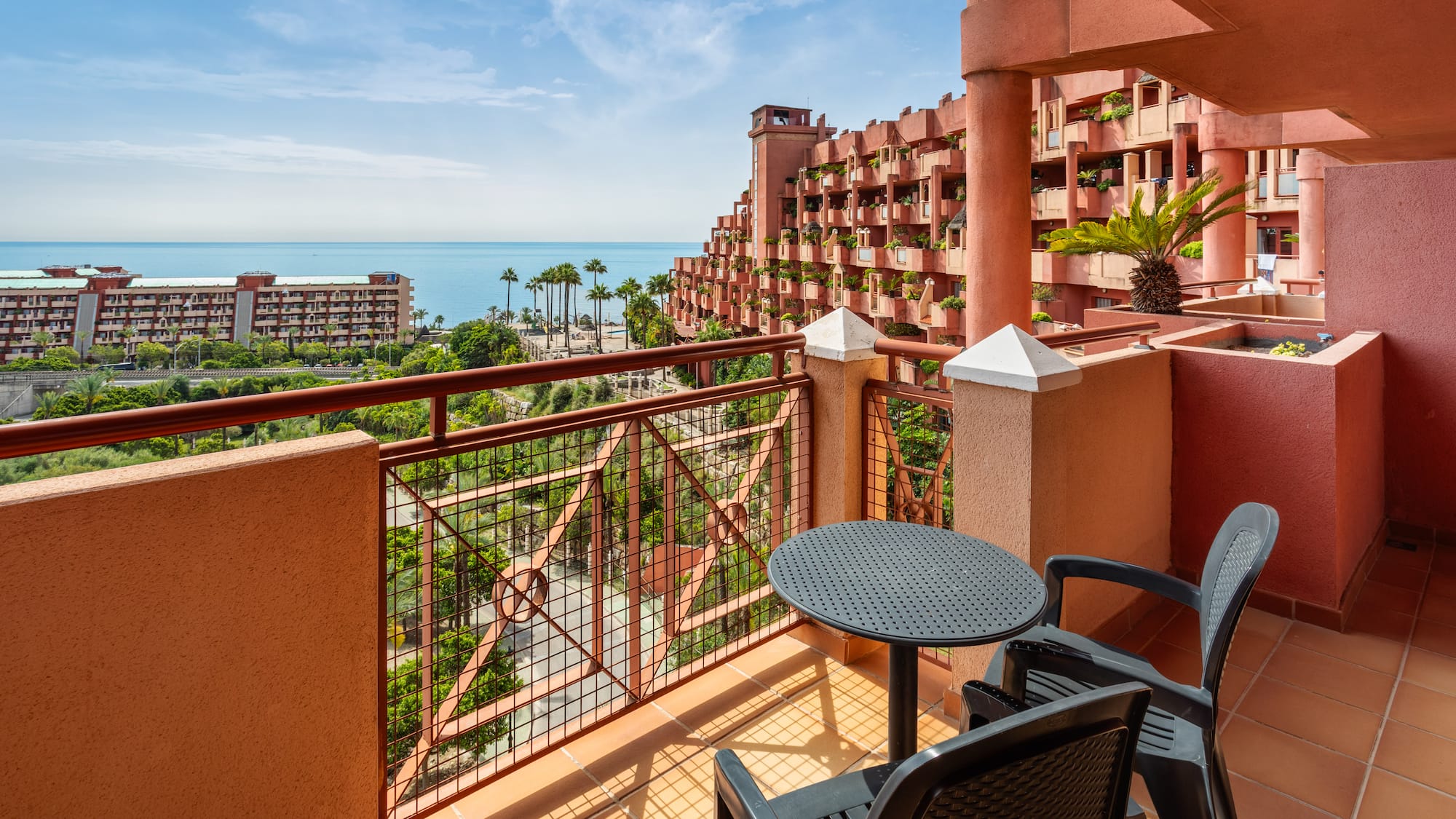 Hotel balcony overlooking Mediterranean sea, unique red resort, palm trees.