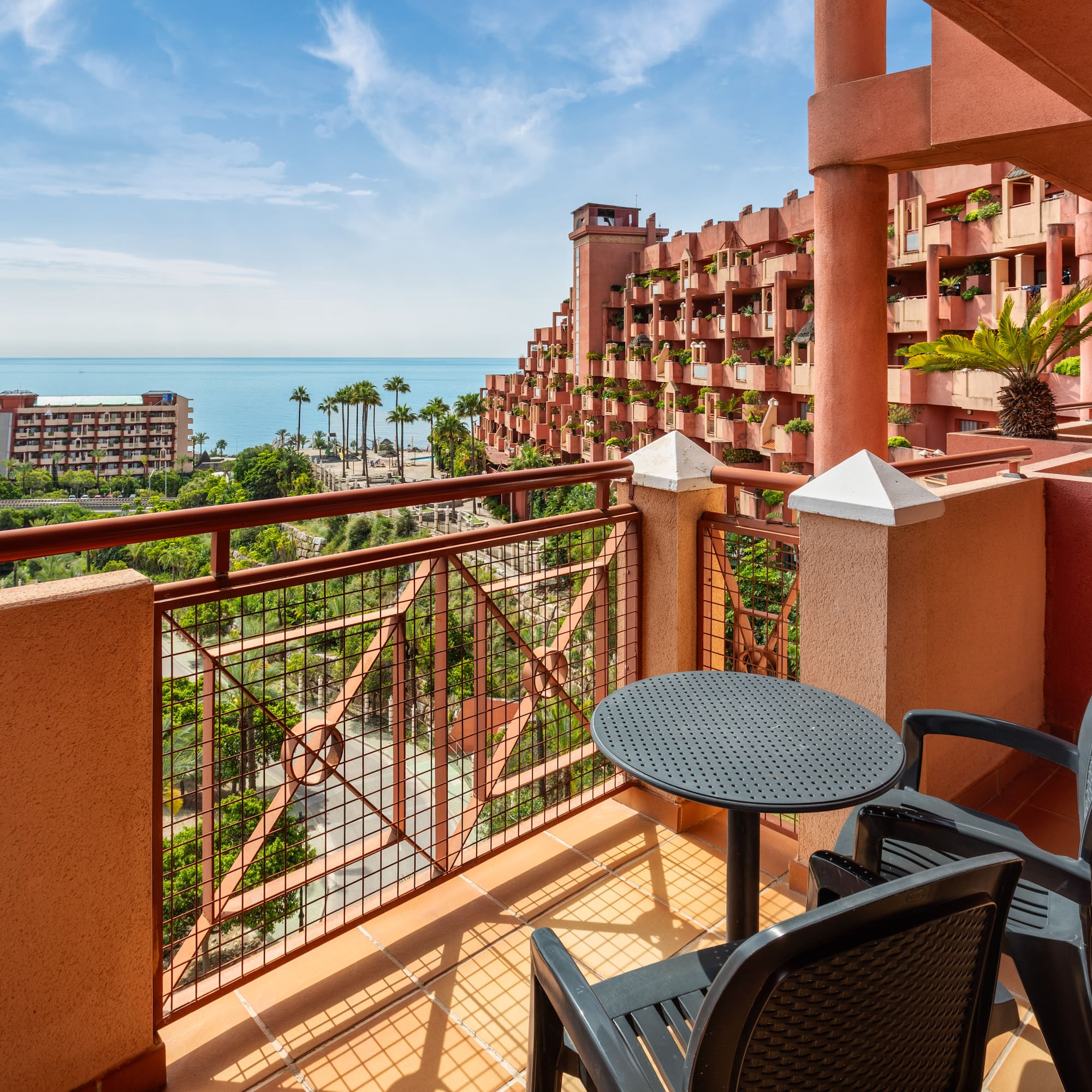 Hotel balcony overlooking Mediterranean sea, unique red resort, palm trees.