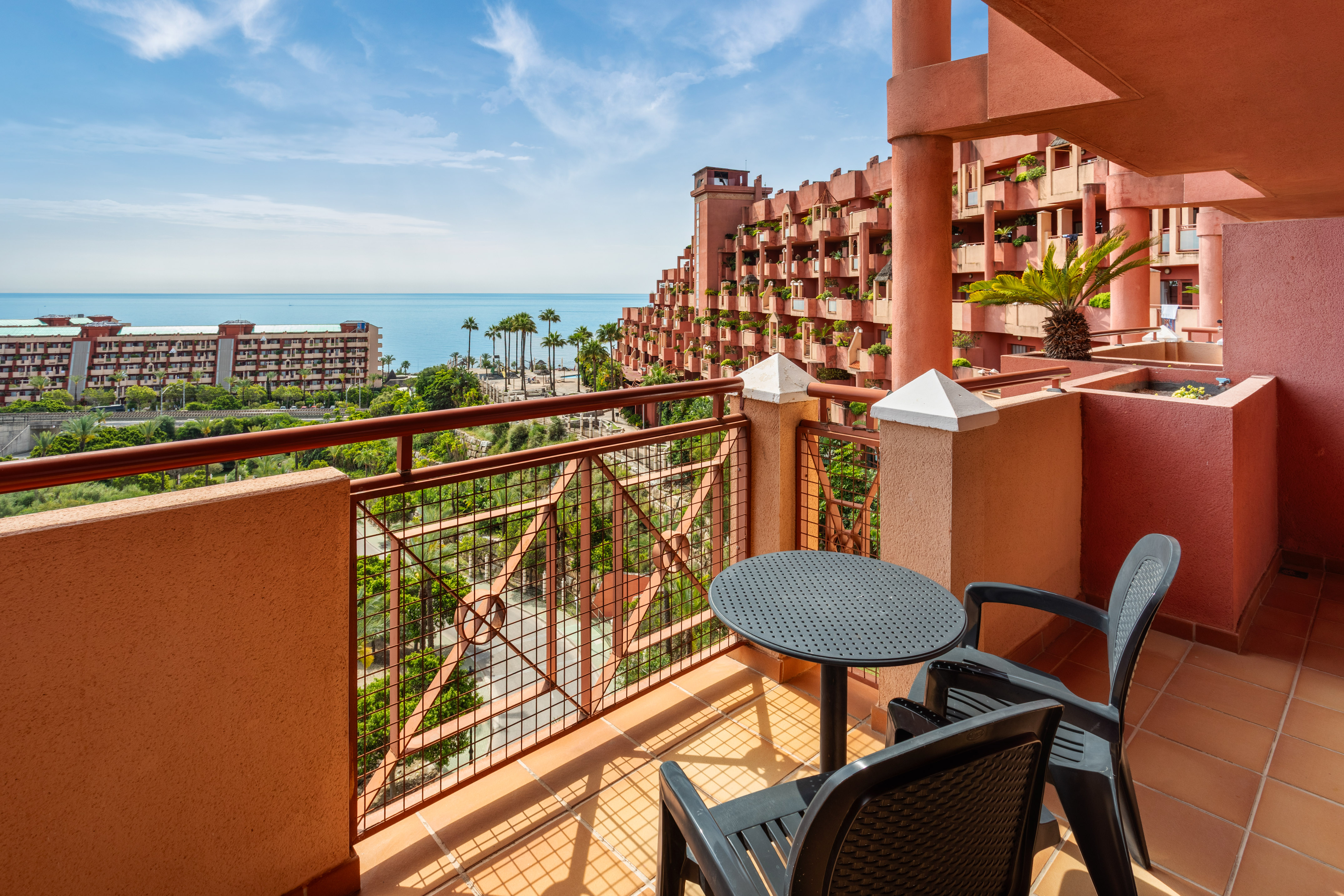 Hotel balcony overlooking the Mediterranean Sea and terraced resort buildings.