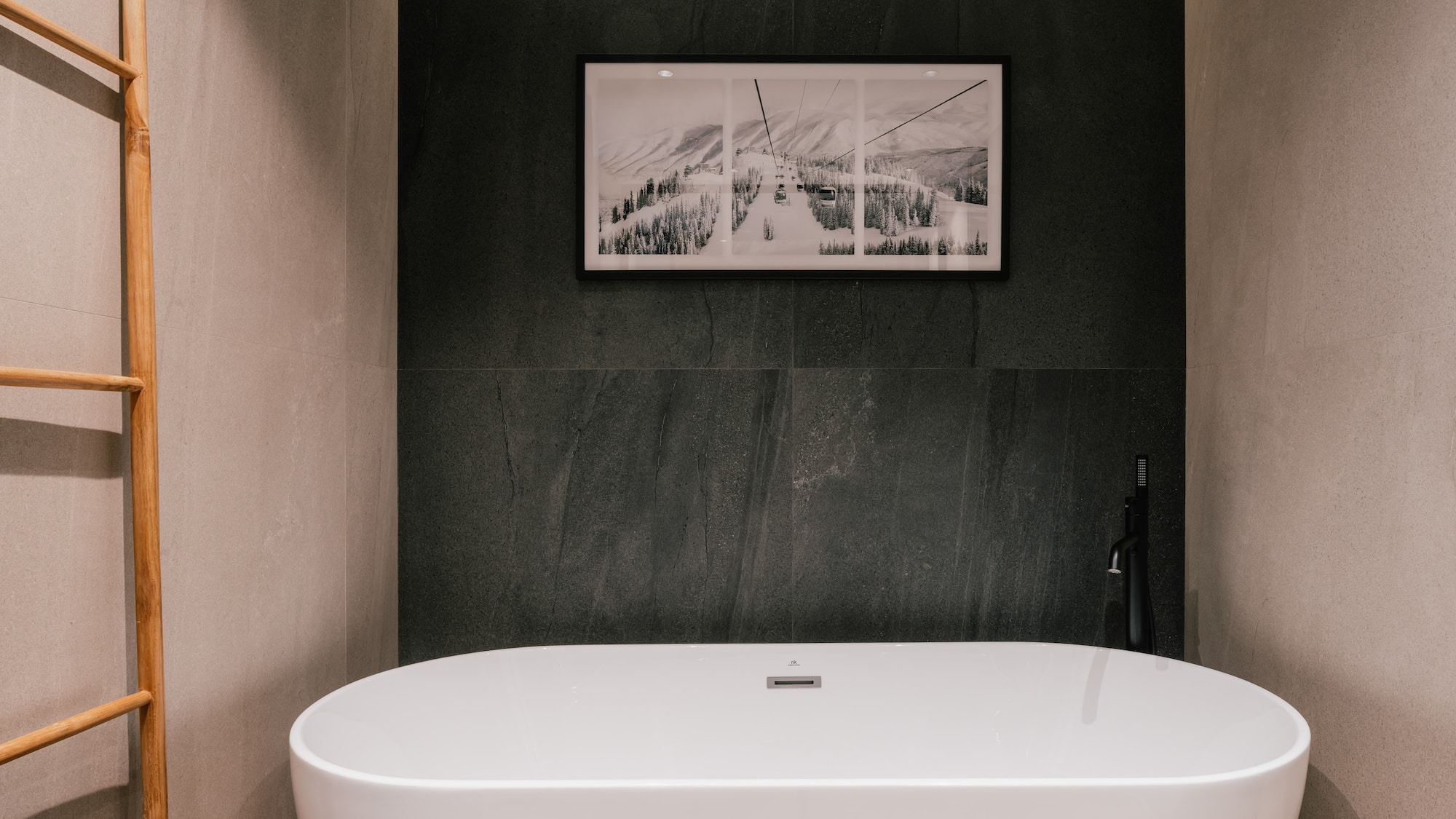 Modern bathroom with white freestanding tub, black faucet, gray tiles, and ski resort wall art.