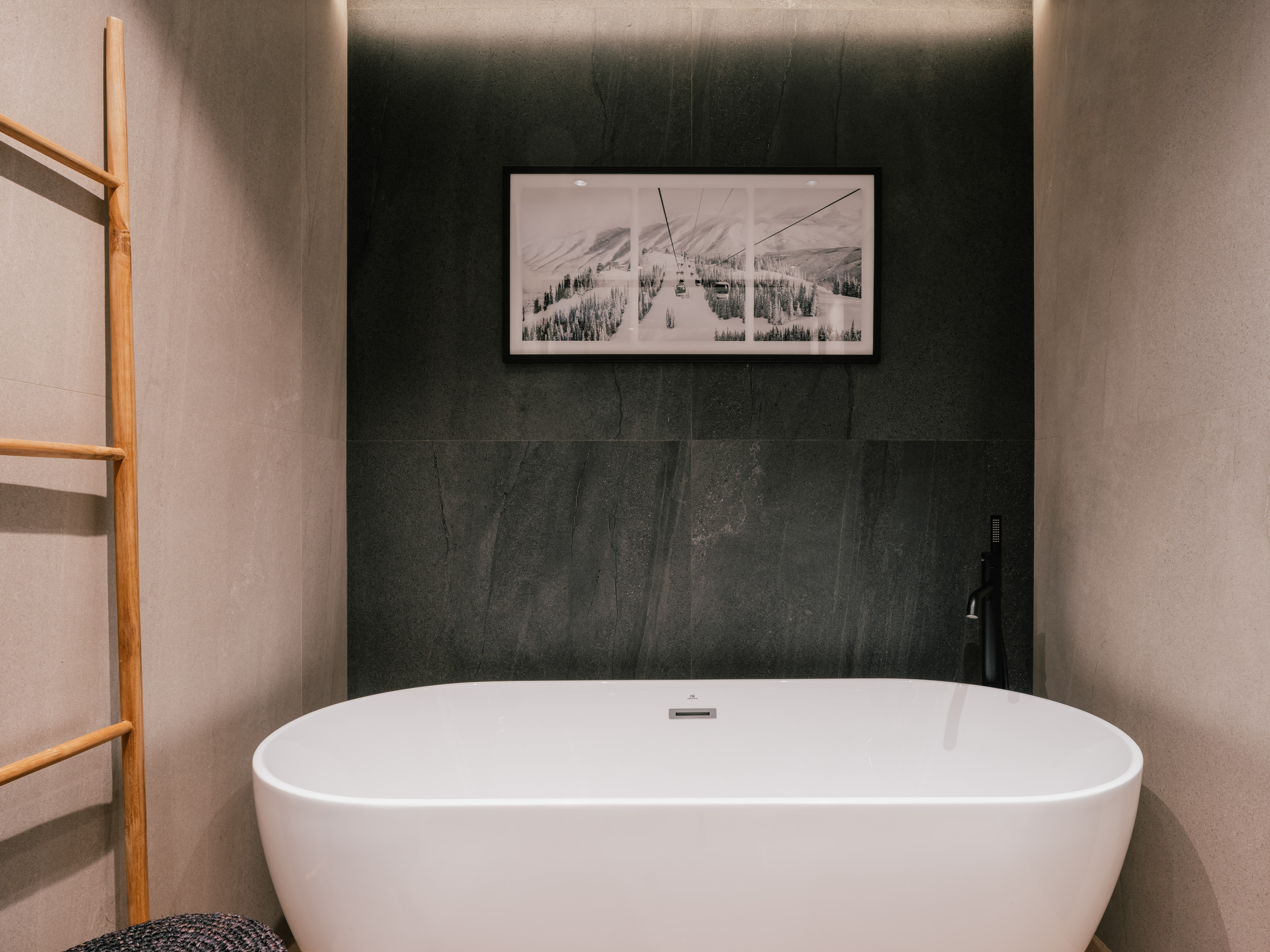Modern bathroom with white freestanding tub, black faucet, gray tiles, and ski resort wall art.