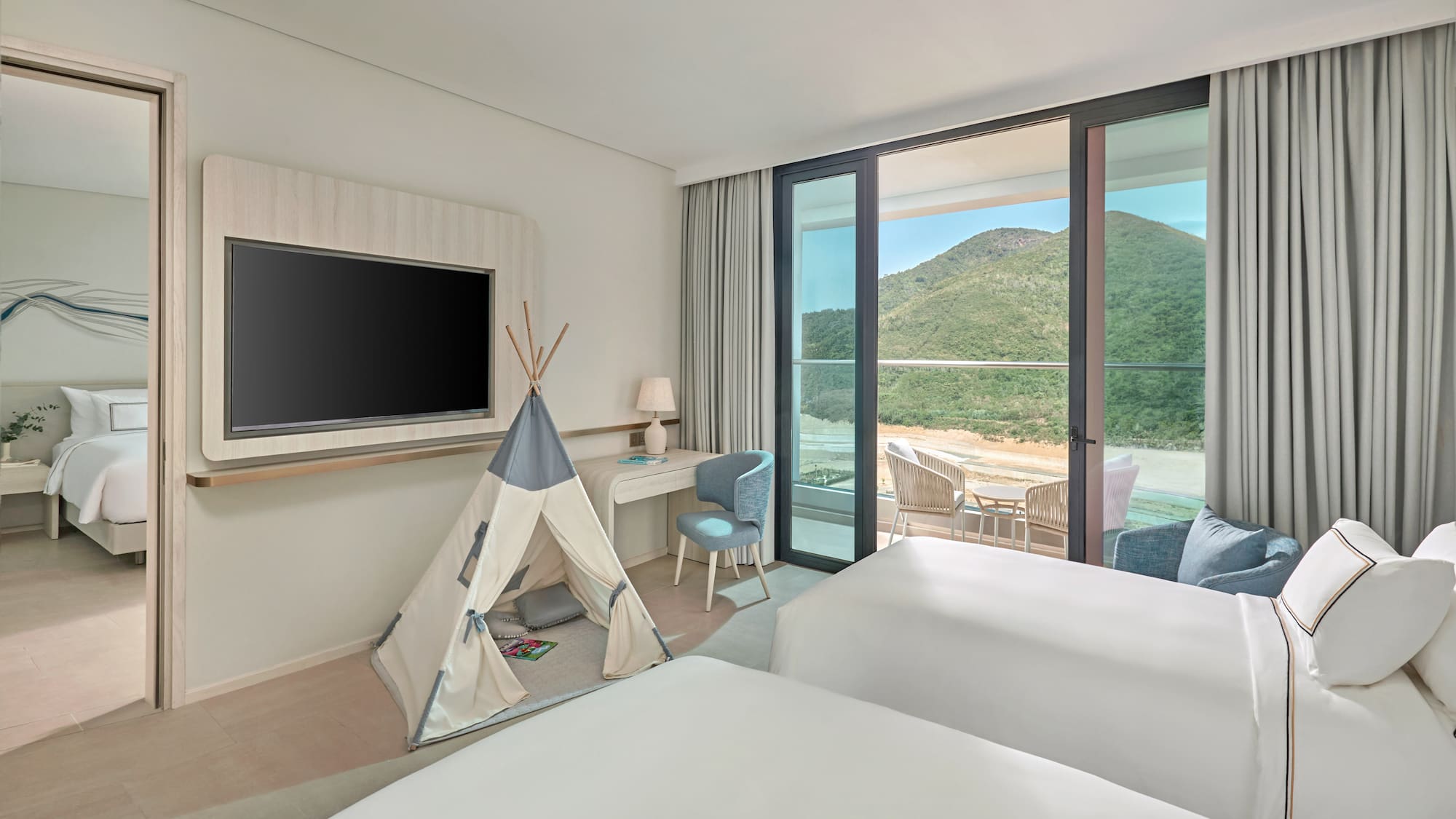 Family hotel room with kids' teepee, two beds, balcony, and mountain view.