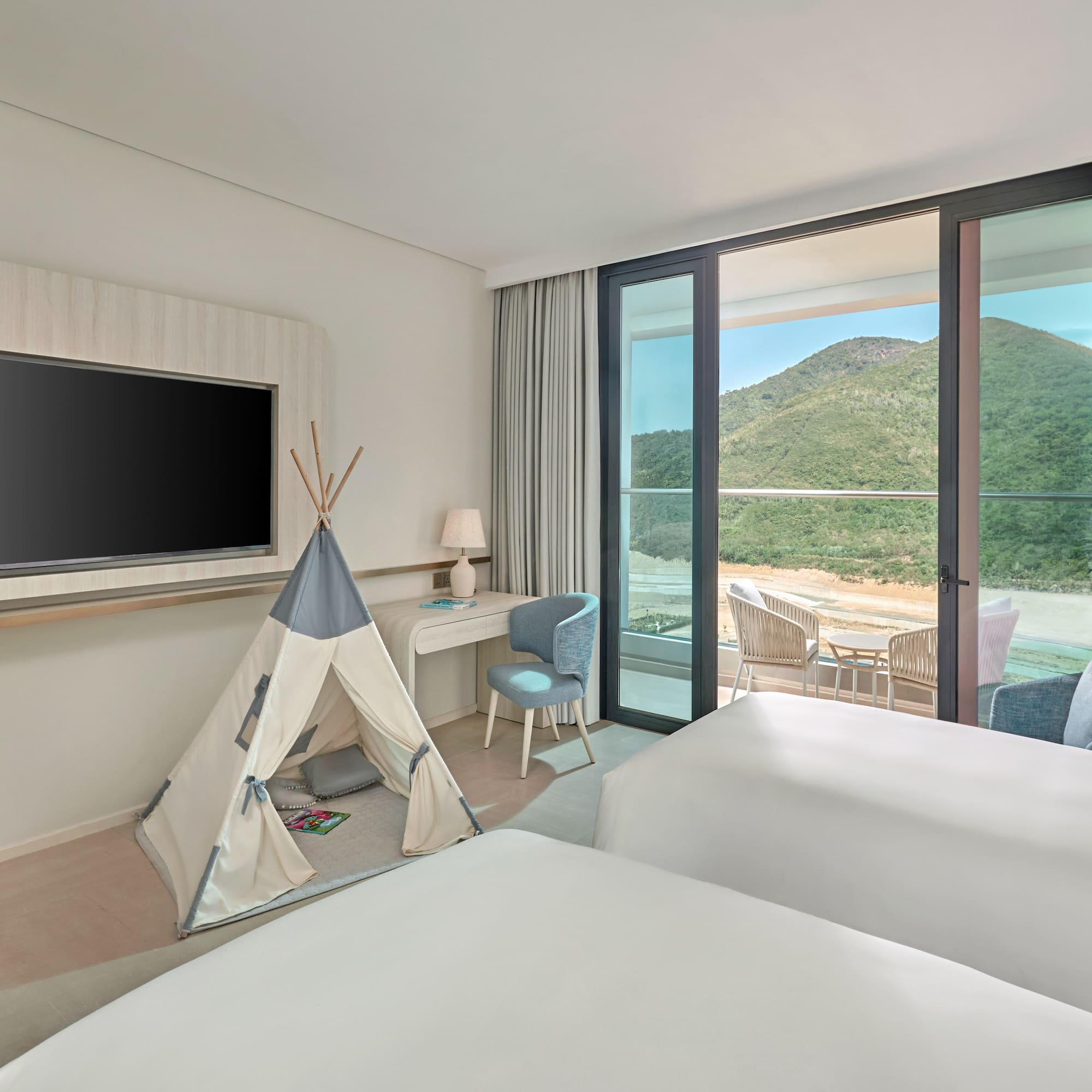 Family hotel room with kids' teepee, two beds, balcony, and mountain view.
