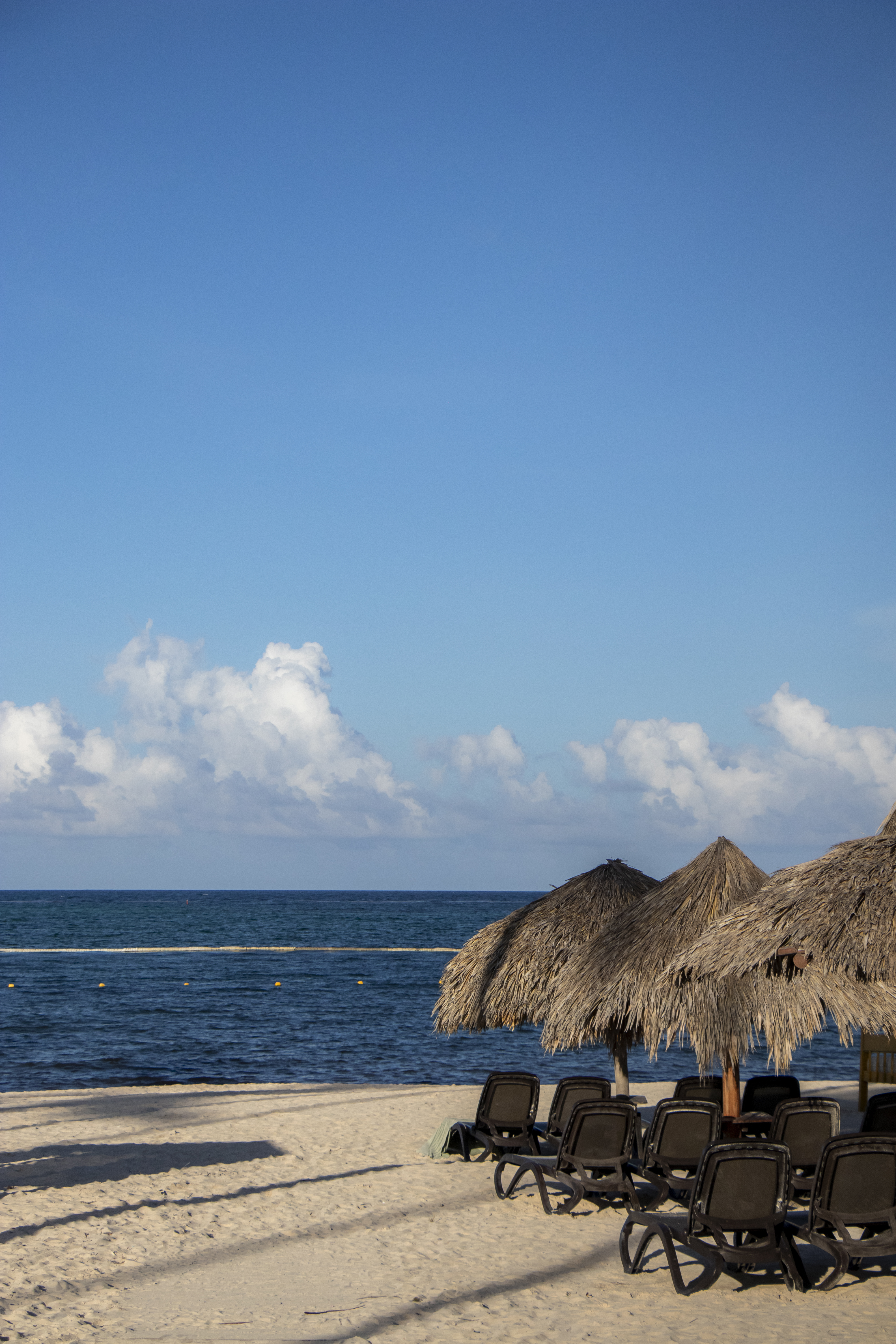 Playa de arena con sombrillas de palapa y tumbonas frente al mar azul.