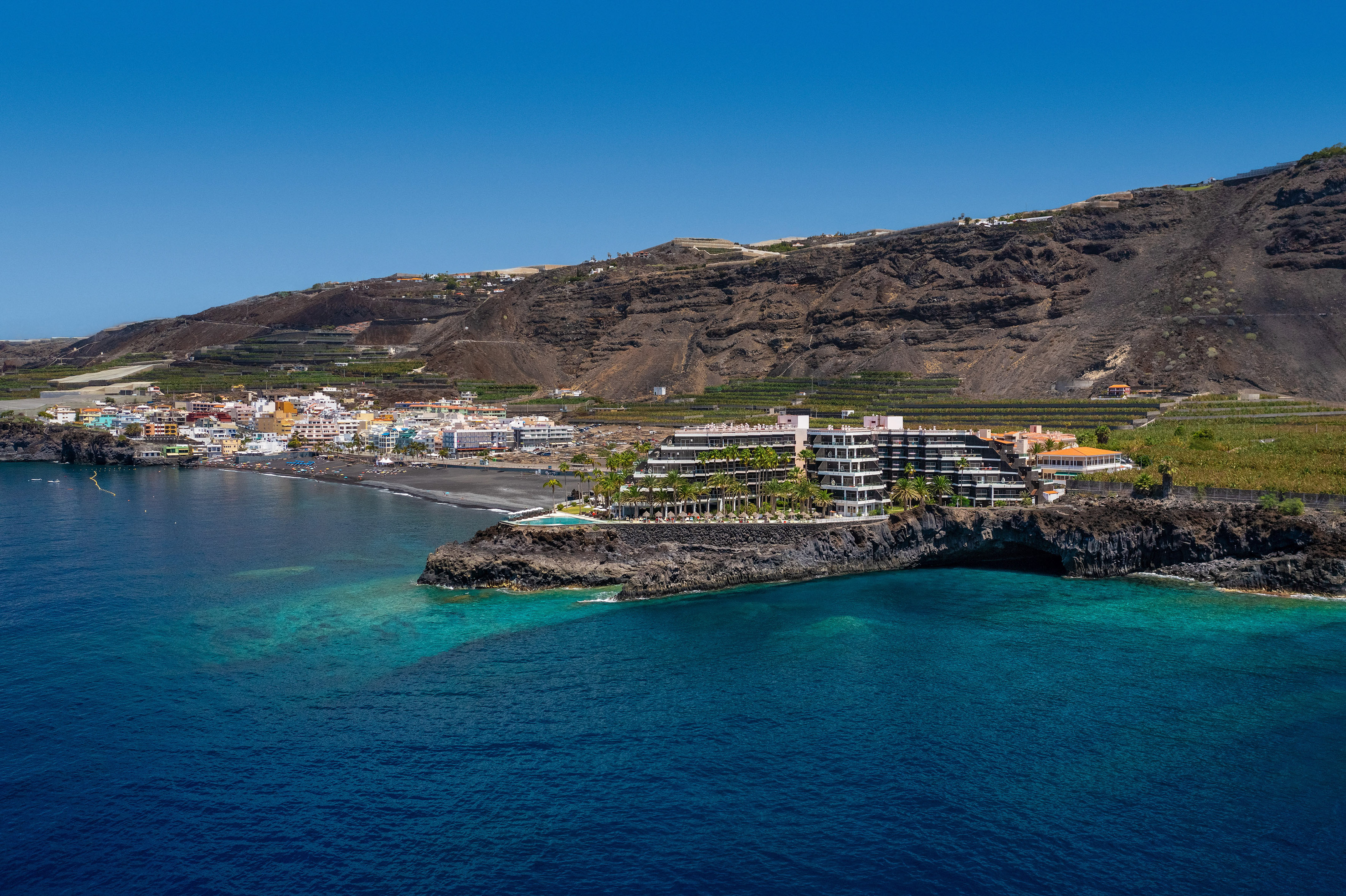 Volcanic island coastal town, resort, black sand beach, and blue ocean.