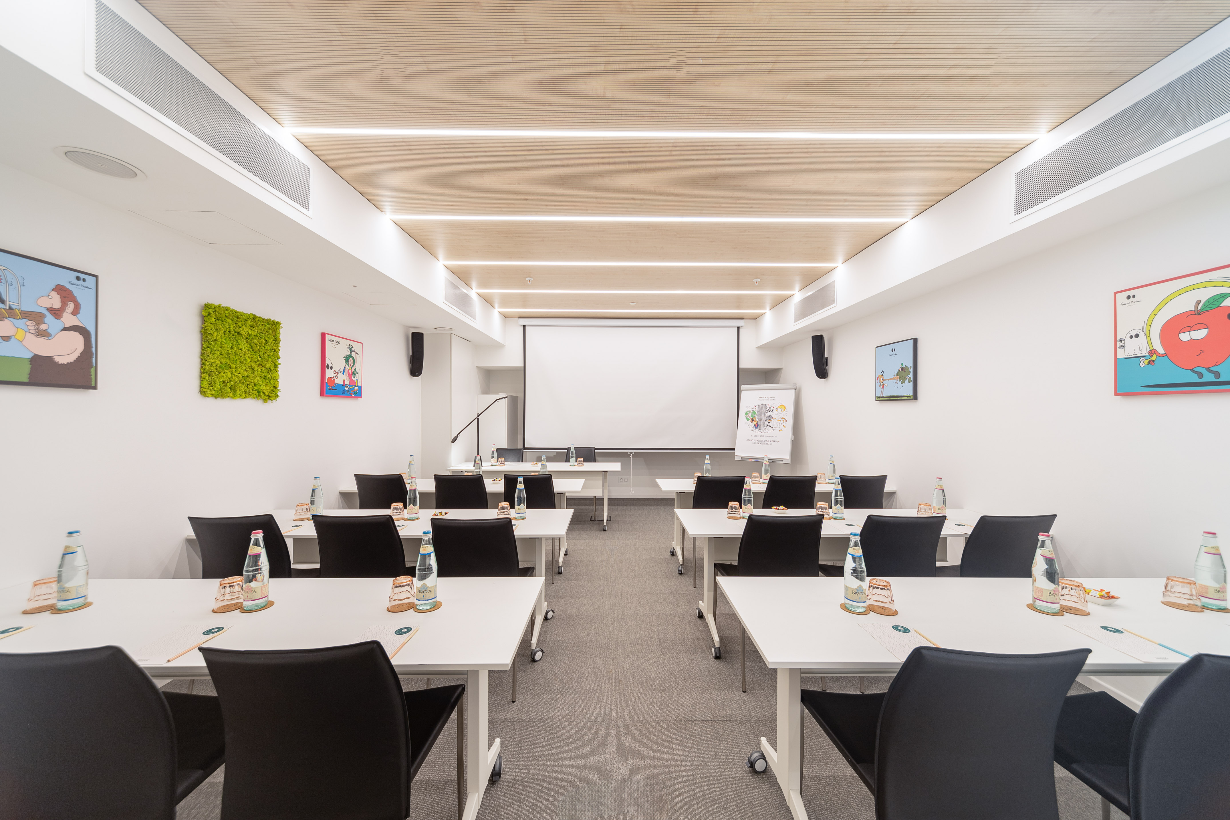 Modern conference room with projector screen, white tables, and colorful art.