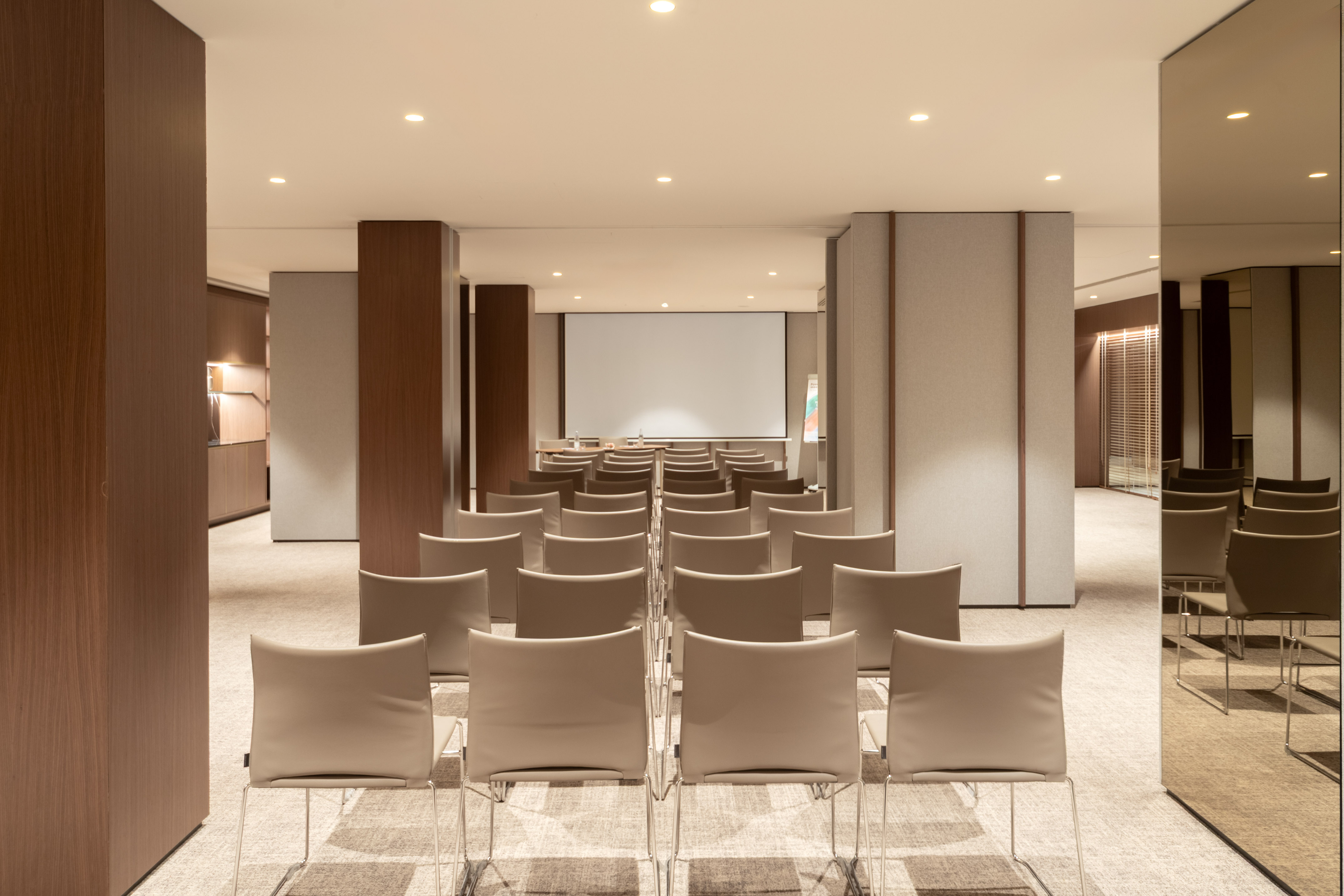 Spacious conference room with beige chairs, projection screen, and warm lighting.