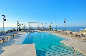 a pool with chairs and a deck chair on a rooftop overlooking the ocean