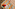 Colorful striped beach towel with red cap, crossword, sunscreen, dominoes on sand.