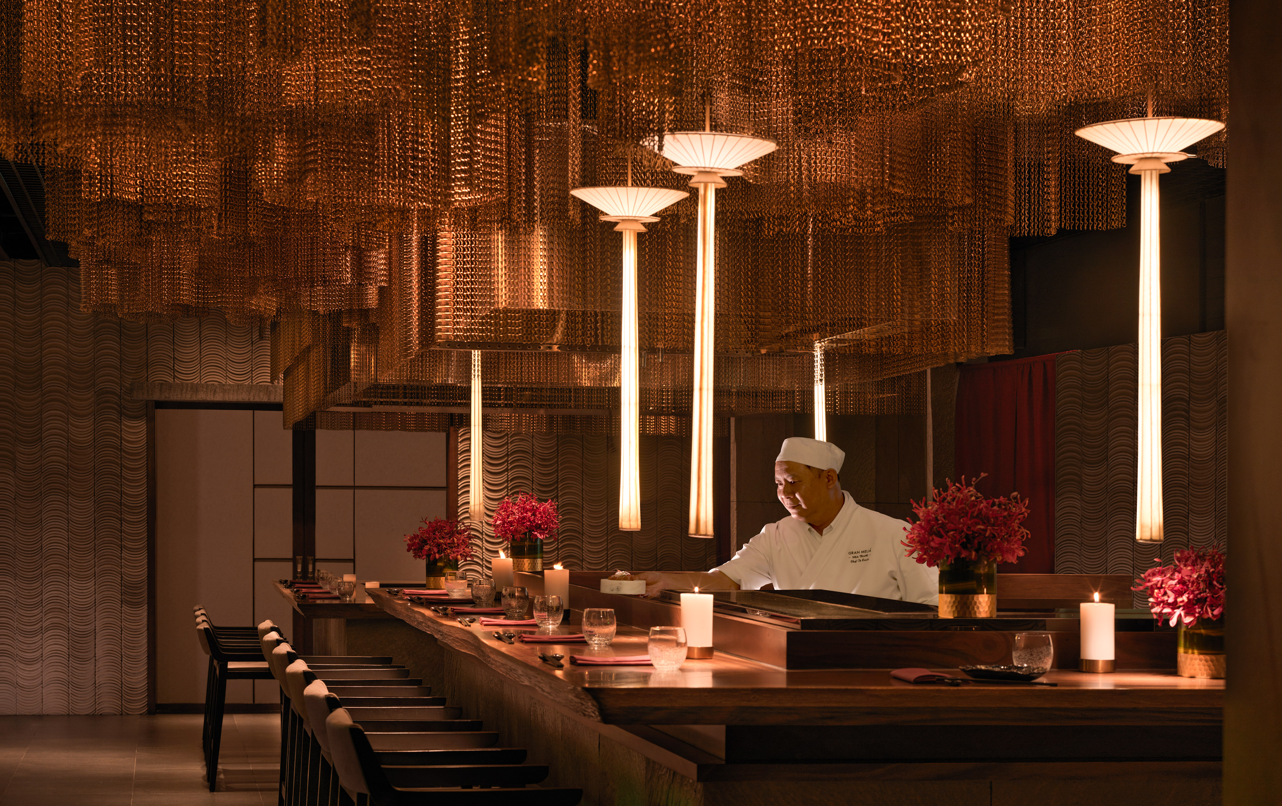 Japanese chef at elegant sushi bar with warm lighting and ornate metallic ceiling.