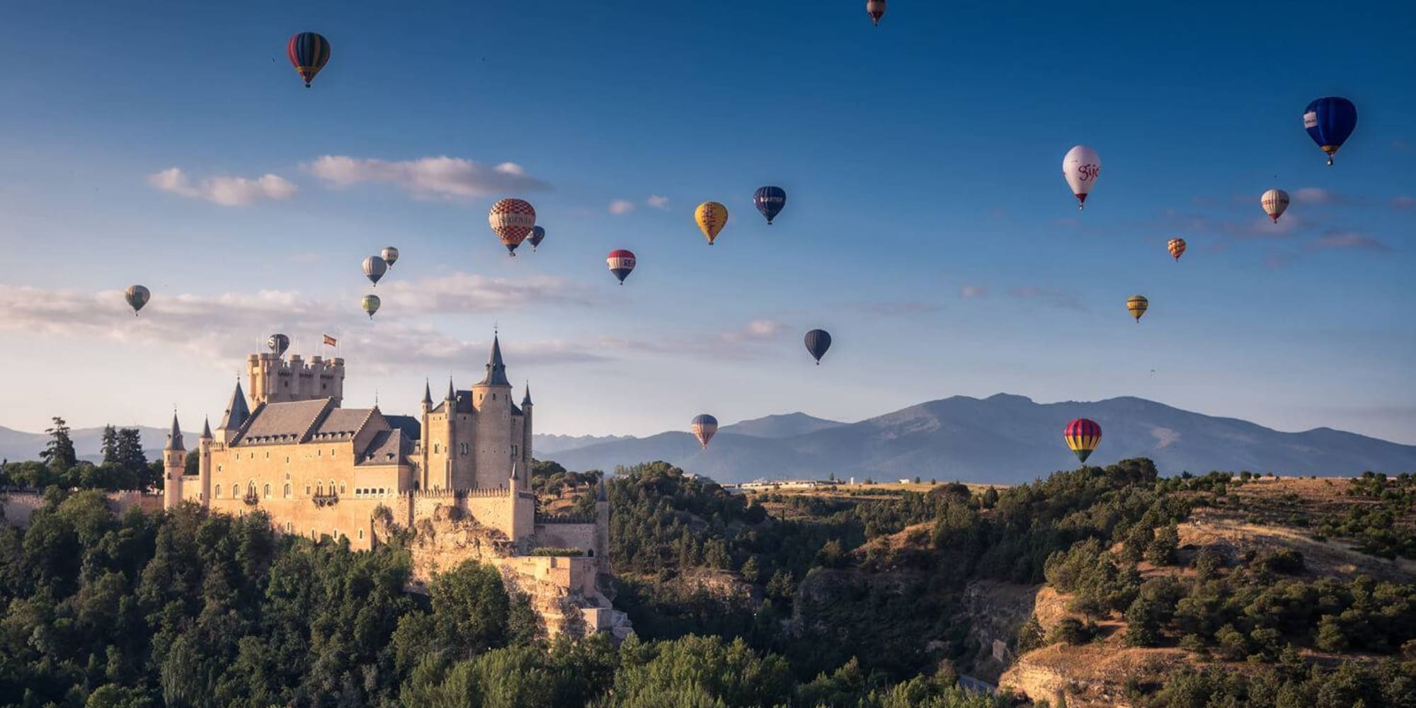 a castle with many hot air balloons flying over a hill