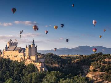 a castle with many hot air balloons flying over a hill