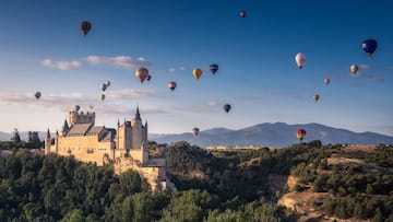 a castle with many hot air balloons flying over a hill