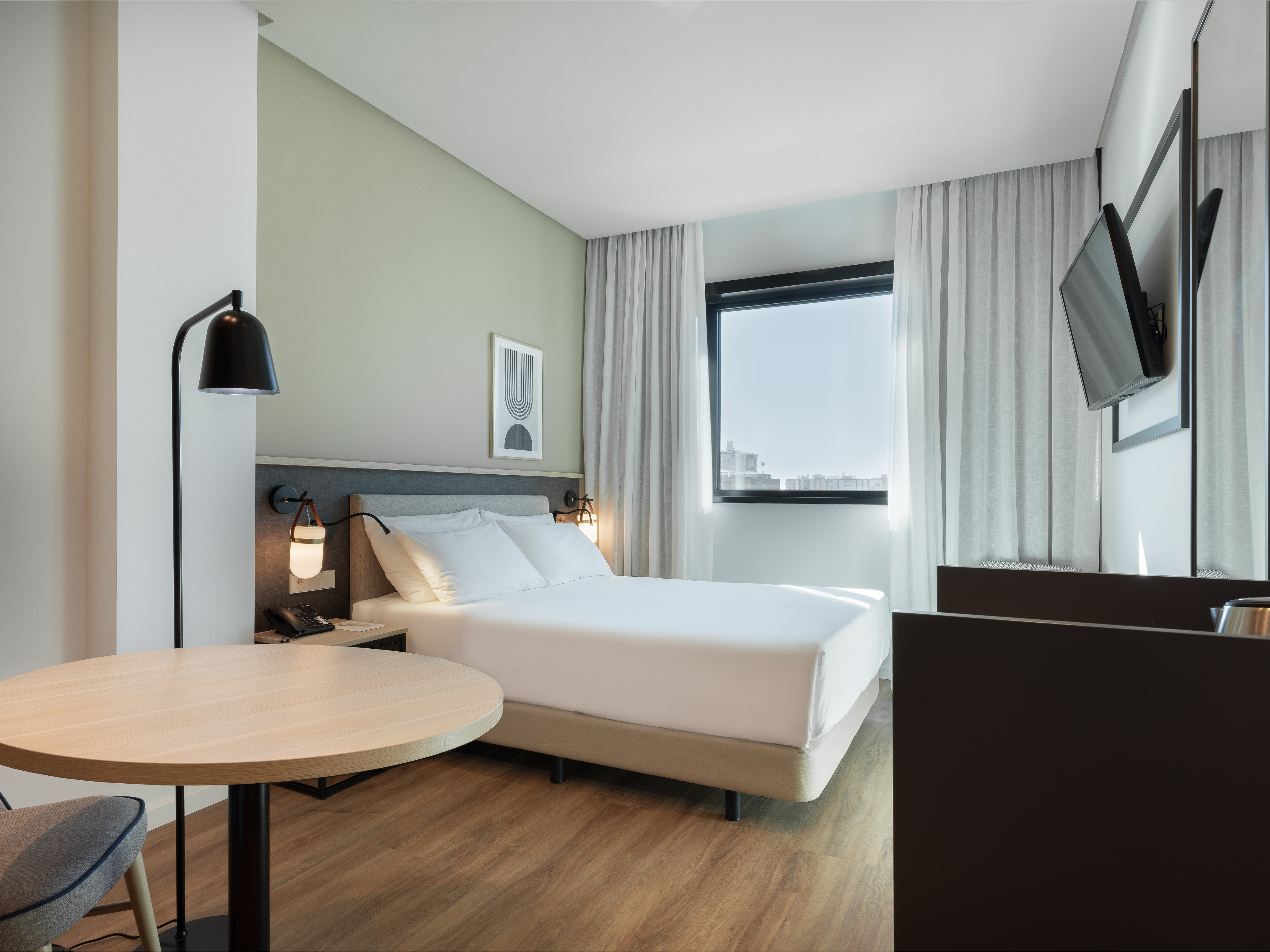 Minimalist hotel bedroom with white bed, wooden floor, large window, and table.