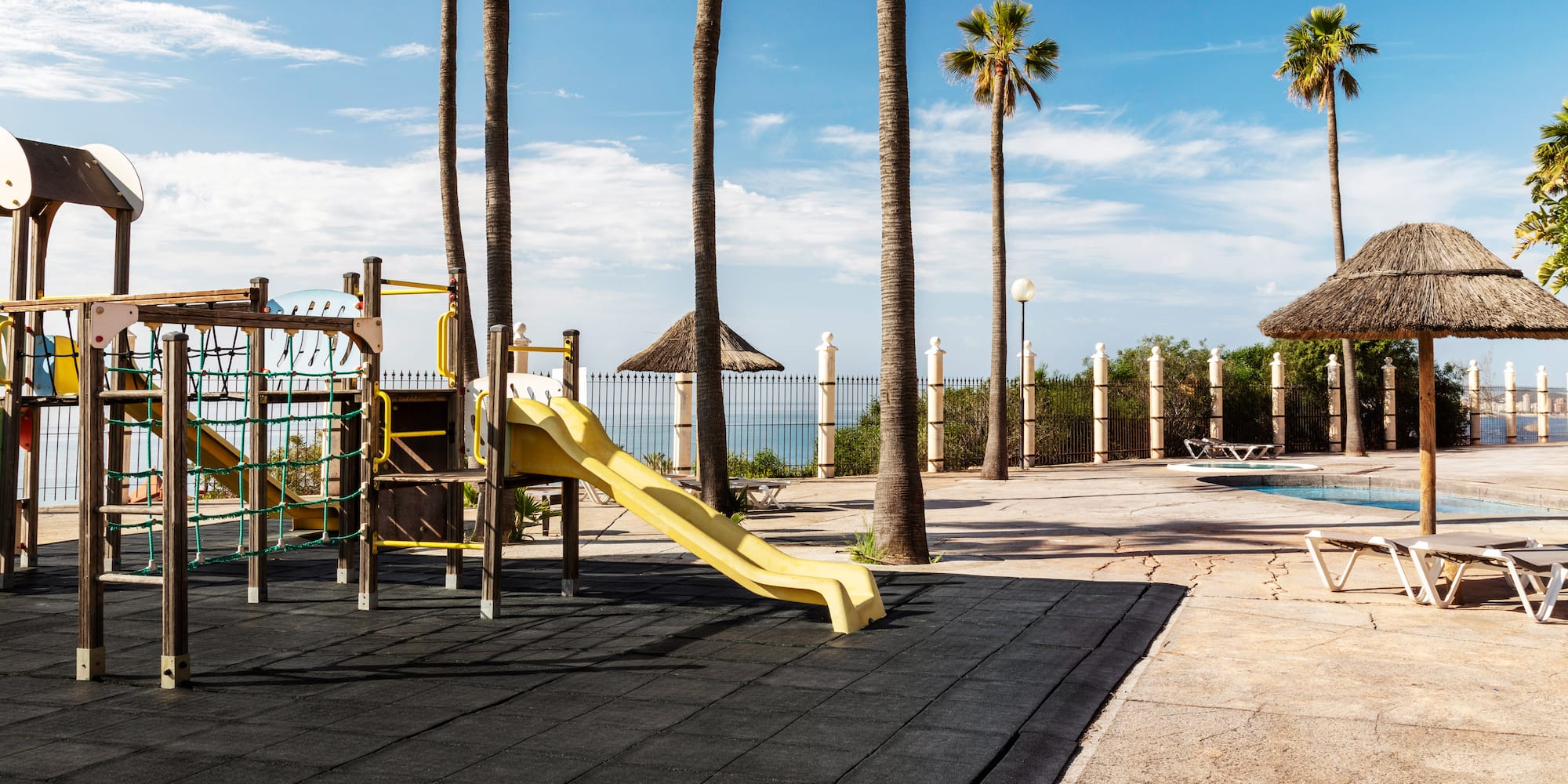 Sunny tropical resort playground with palm trees and pool.