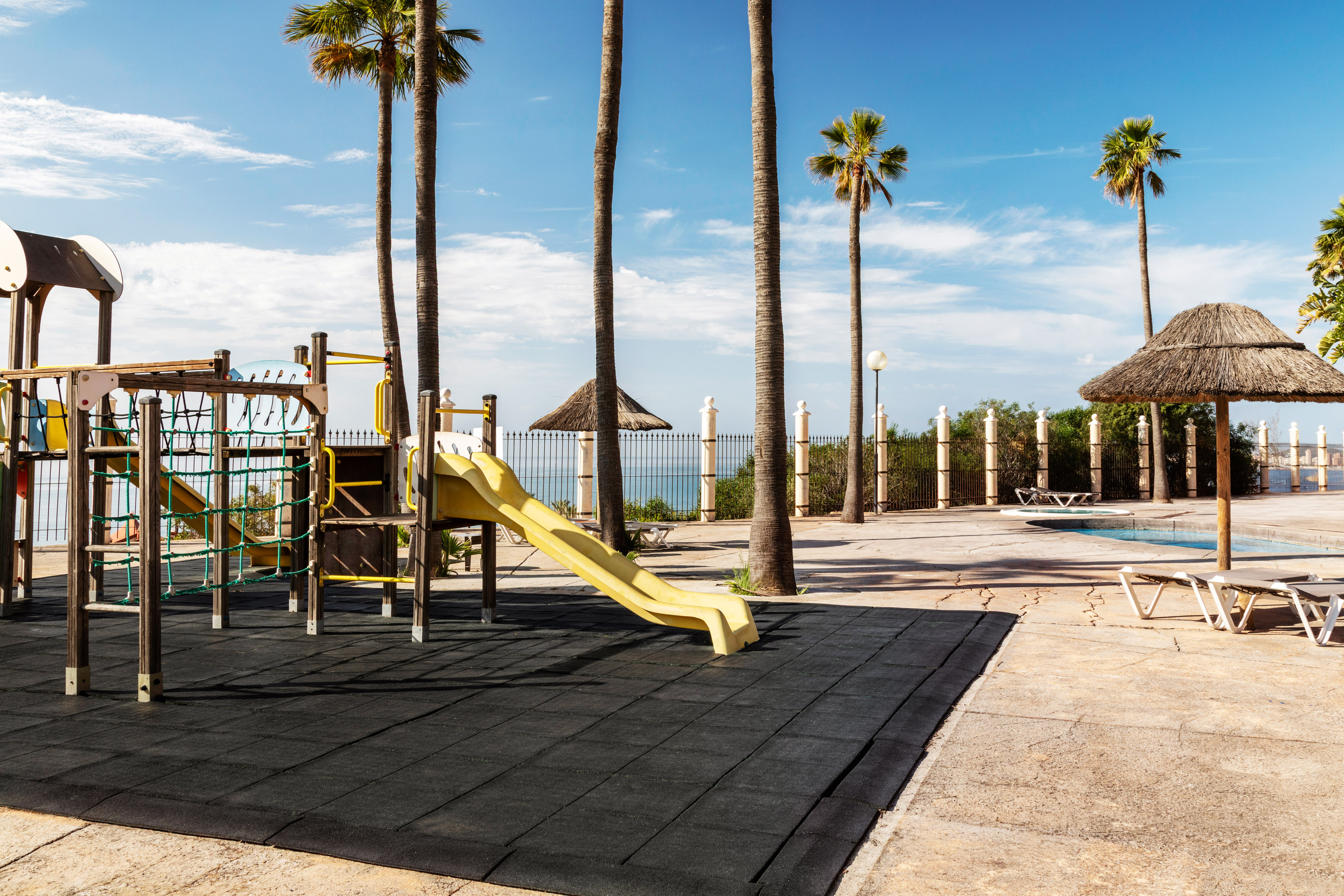 Sunny tropical resort playground with palm trees and pool.