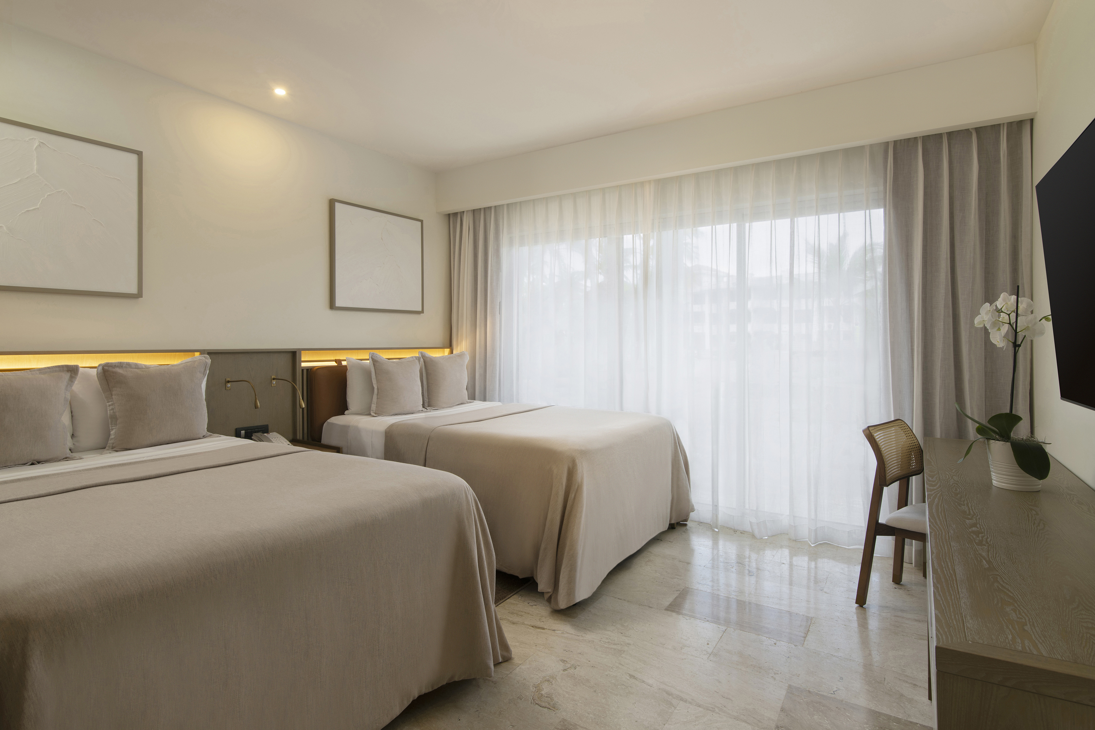 Modern hotel room with two beds, neutral decor, sheer curtains, and light tile floor.