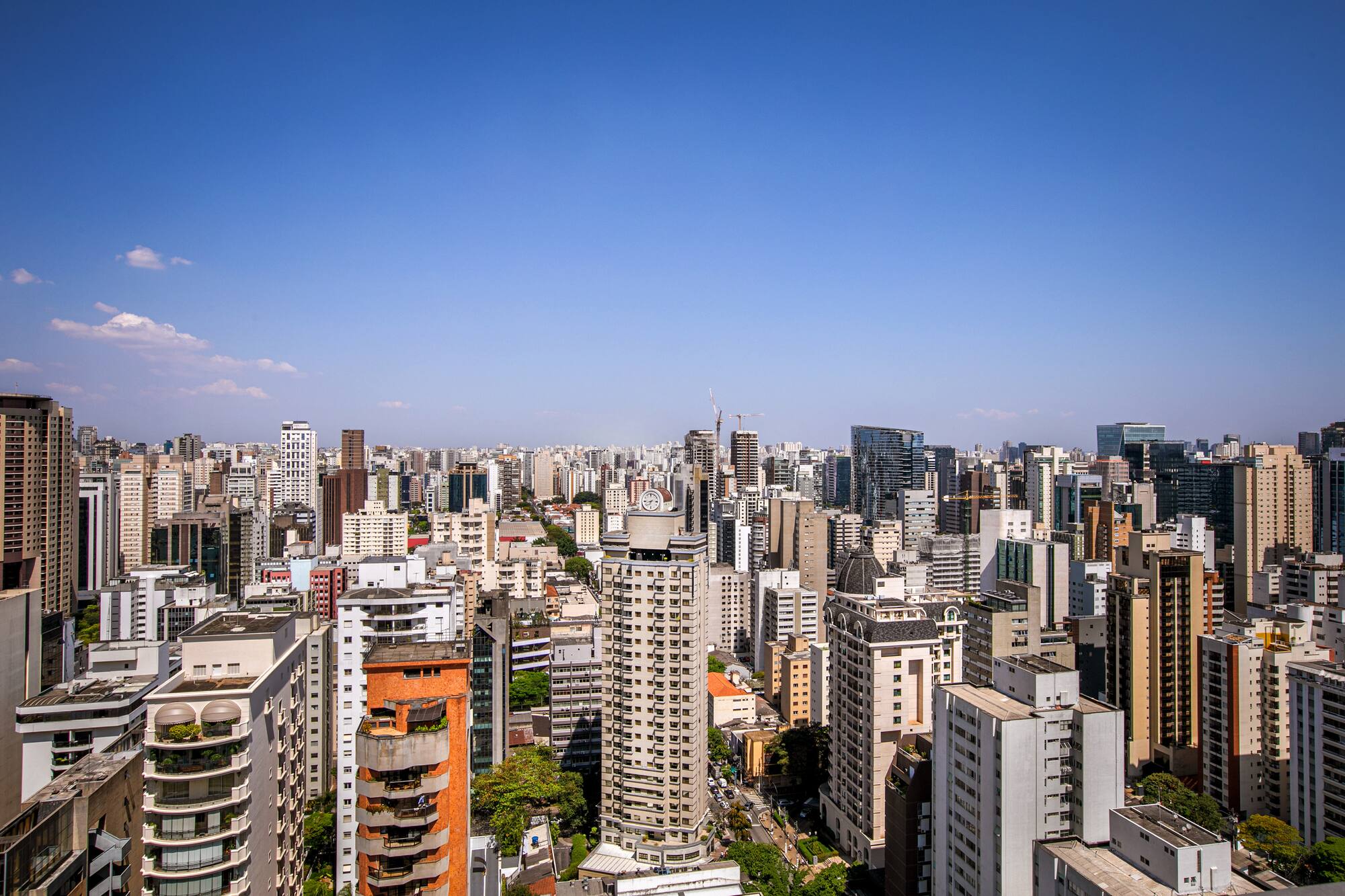 Dense city skyline of residential and commercial high-rises, clear blue sky.