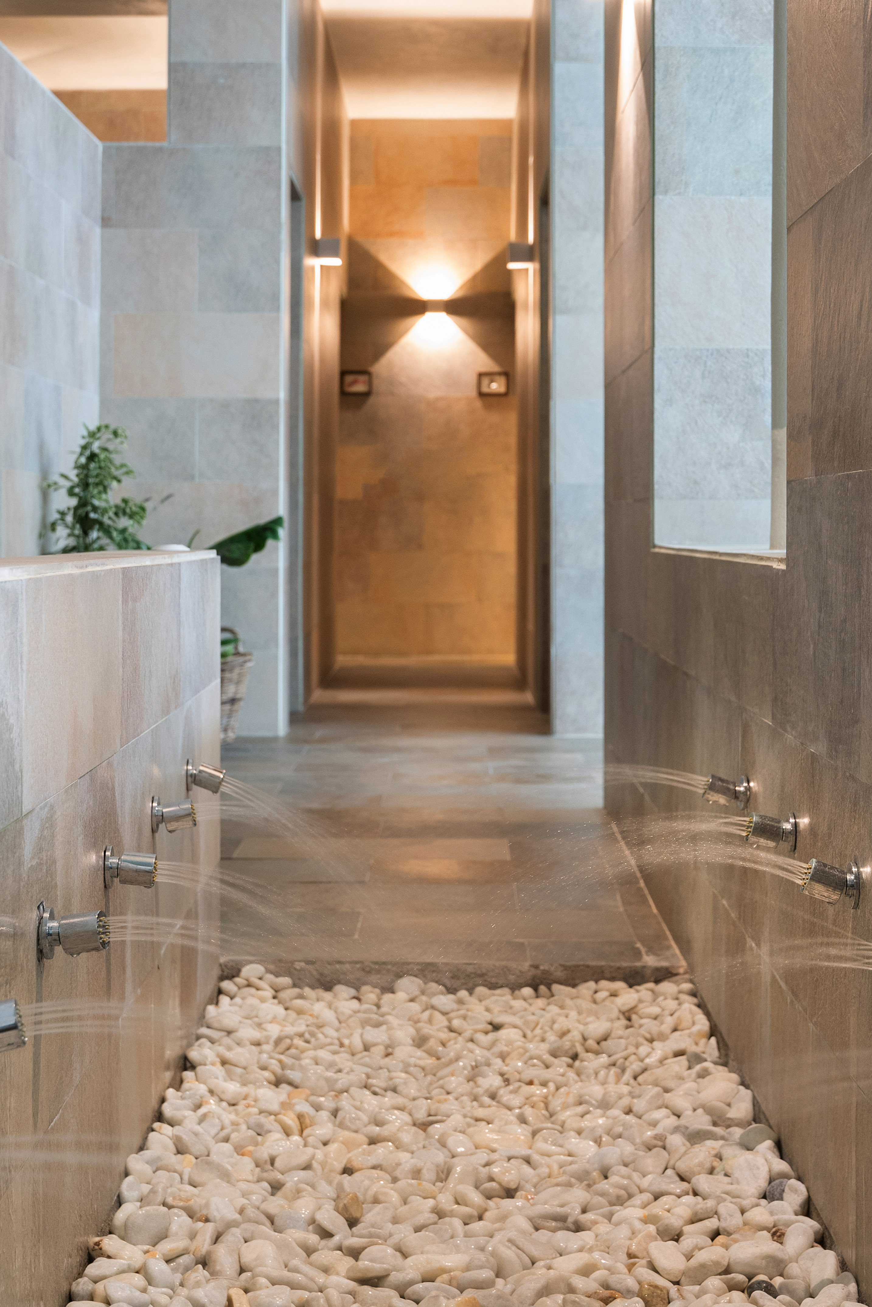 Modern spa shower with active body jets, white pebble floor, and warm lighting.