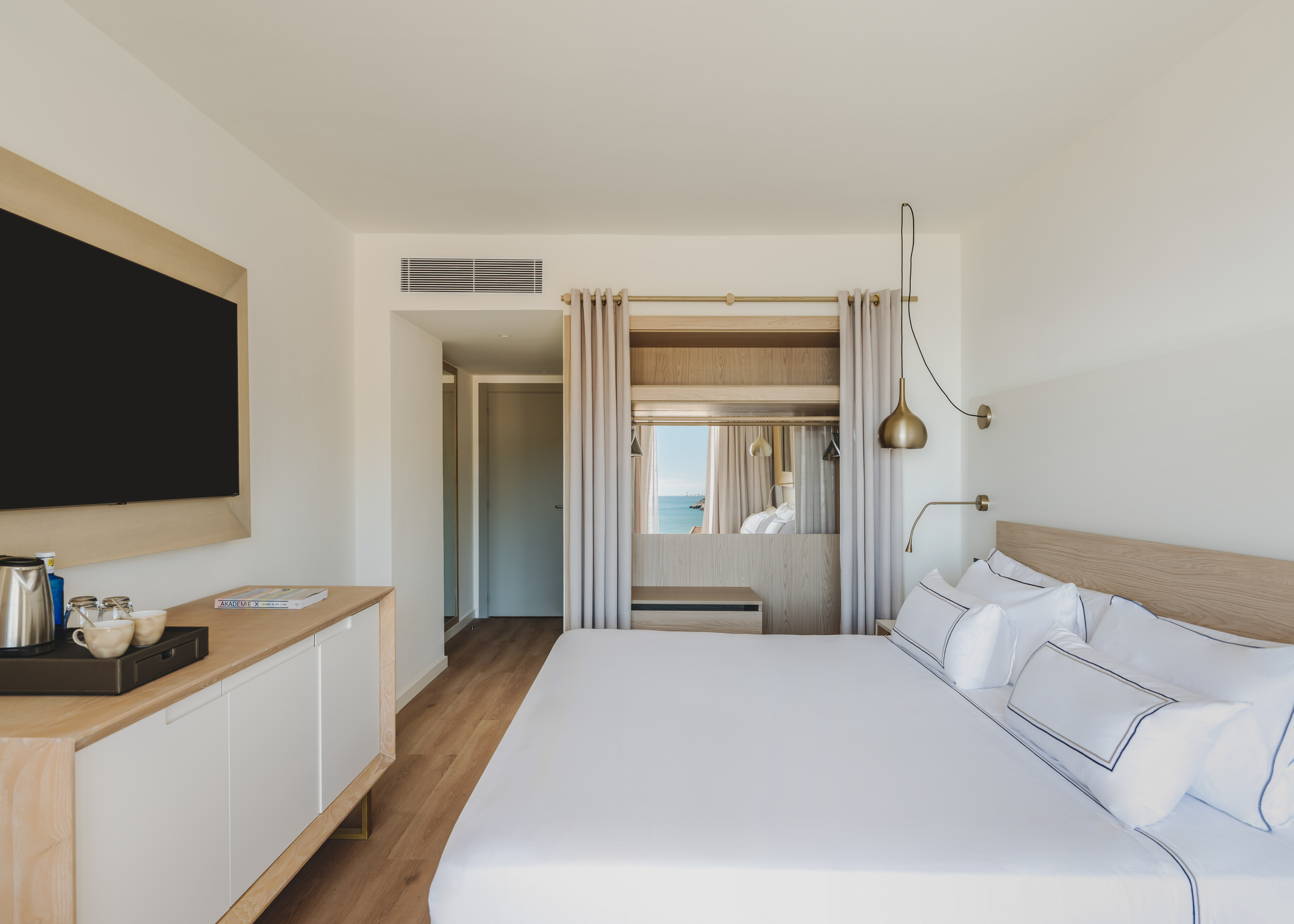 Modern hotel room with ocean view, white bed, wooden furniture, and sleek TV.