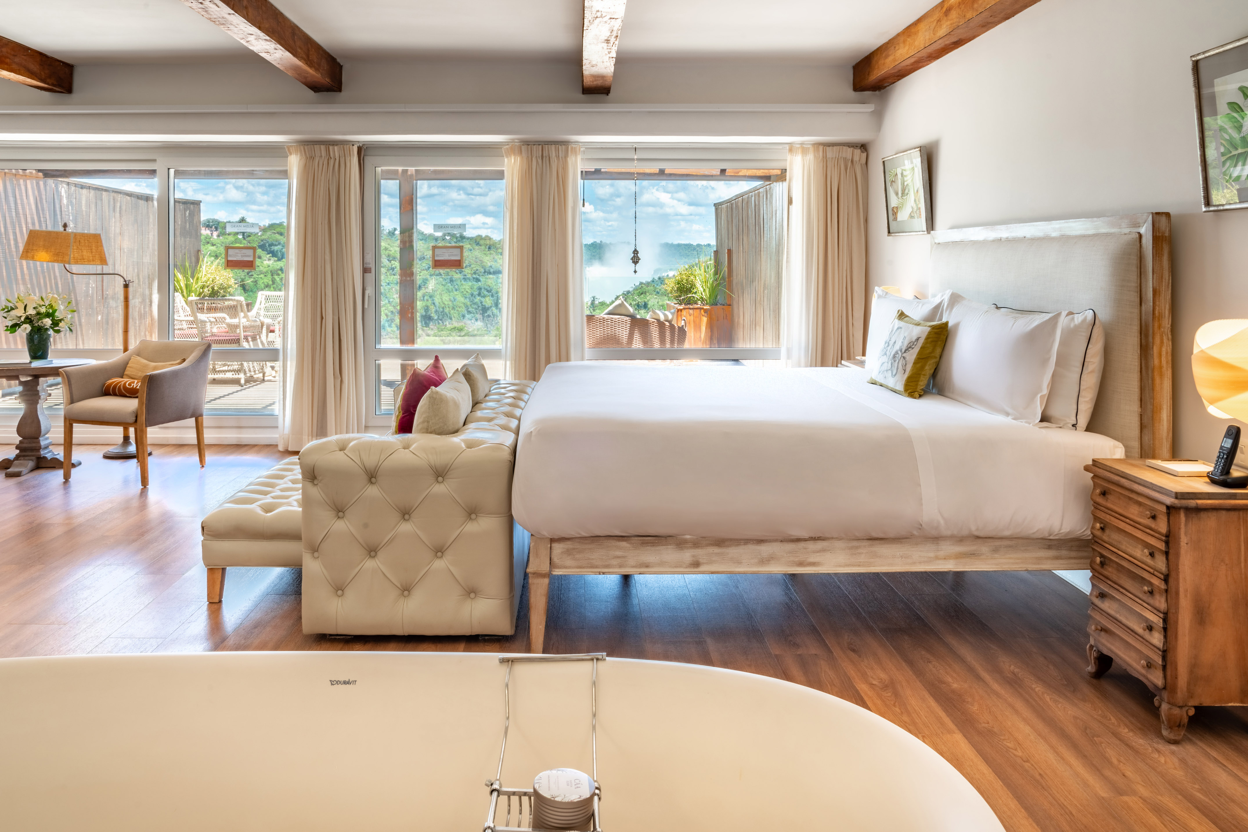 Hotel room with bed, bathtub, and large windows overlooking a scenic waterfall.