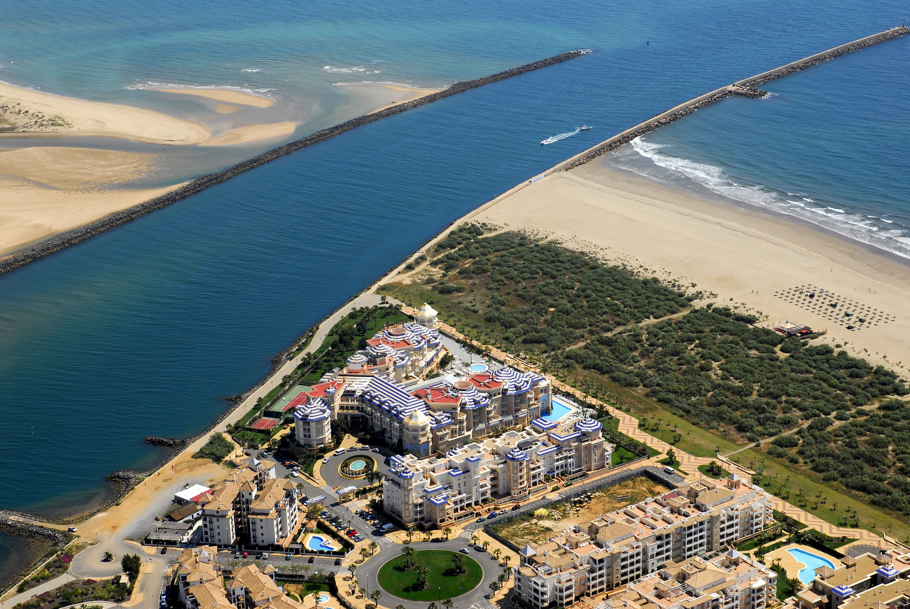 Aerial view: Large coastal resort, sandy beaches, long jetty, and channel.