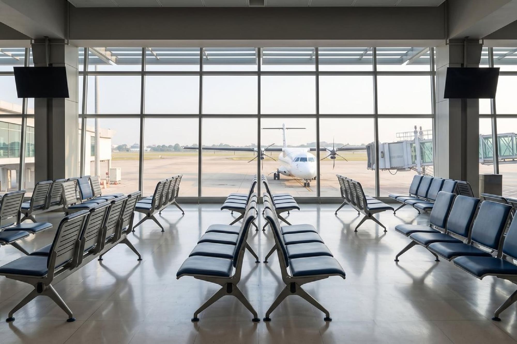 Empty airport gate waiting area with blue seats and airplane on tarmac.