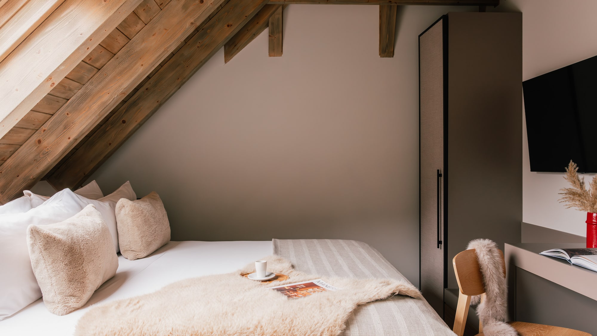 Cozy attic bedroom with exposed wooden beams, plush bed, and modern decor.