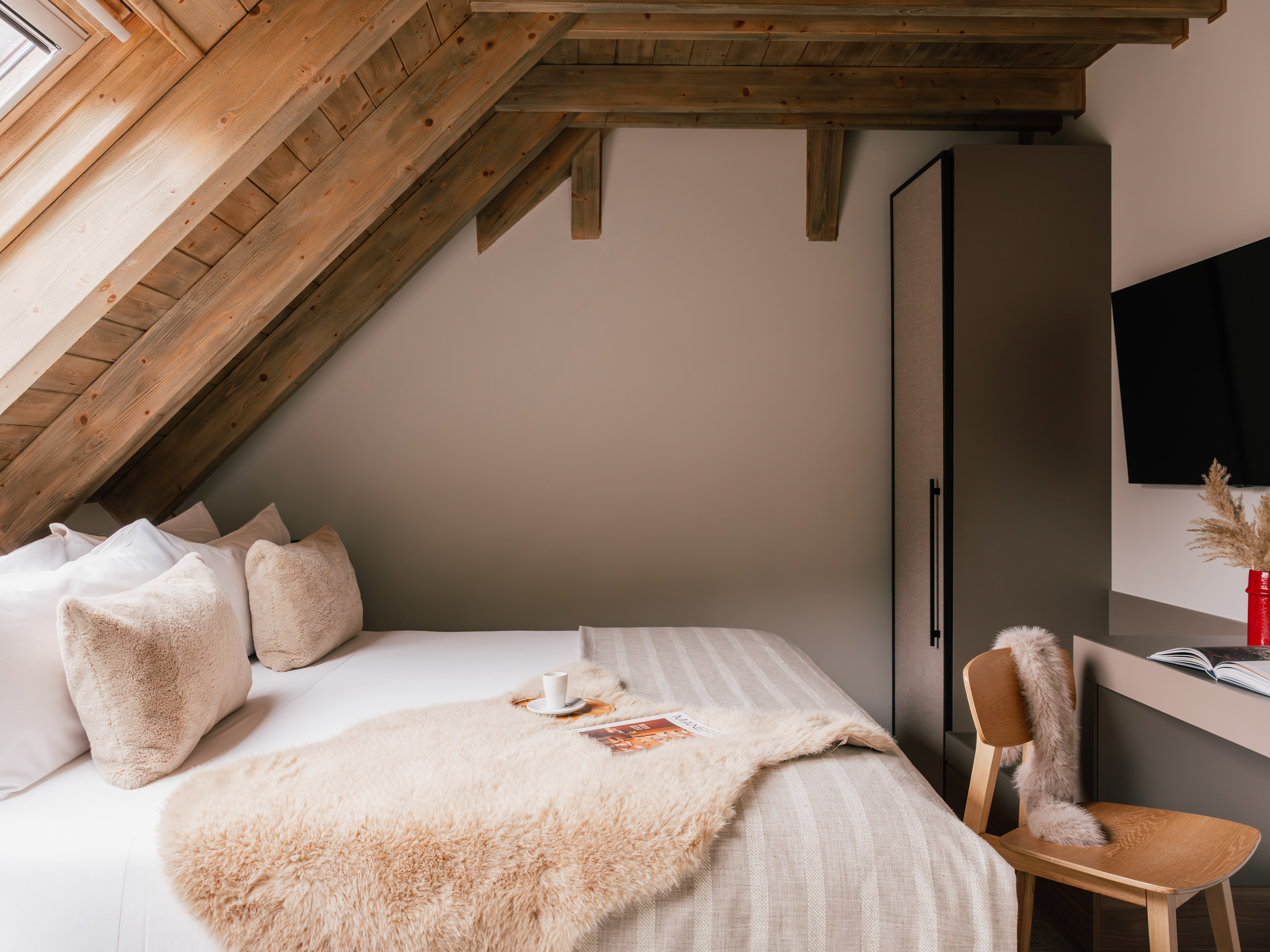 Cozy attic bedroom with exposed wooden beams, plush bed, and modern decor.