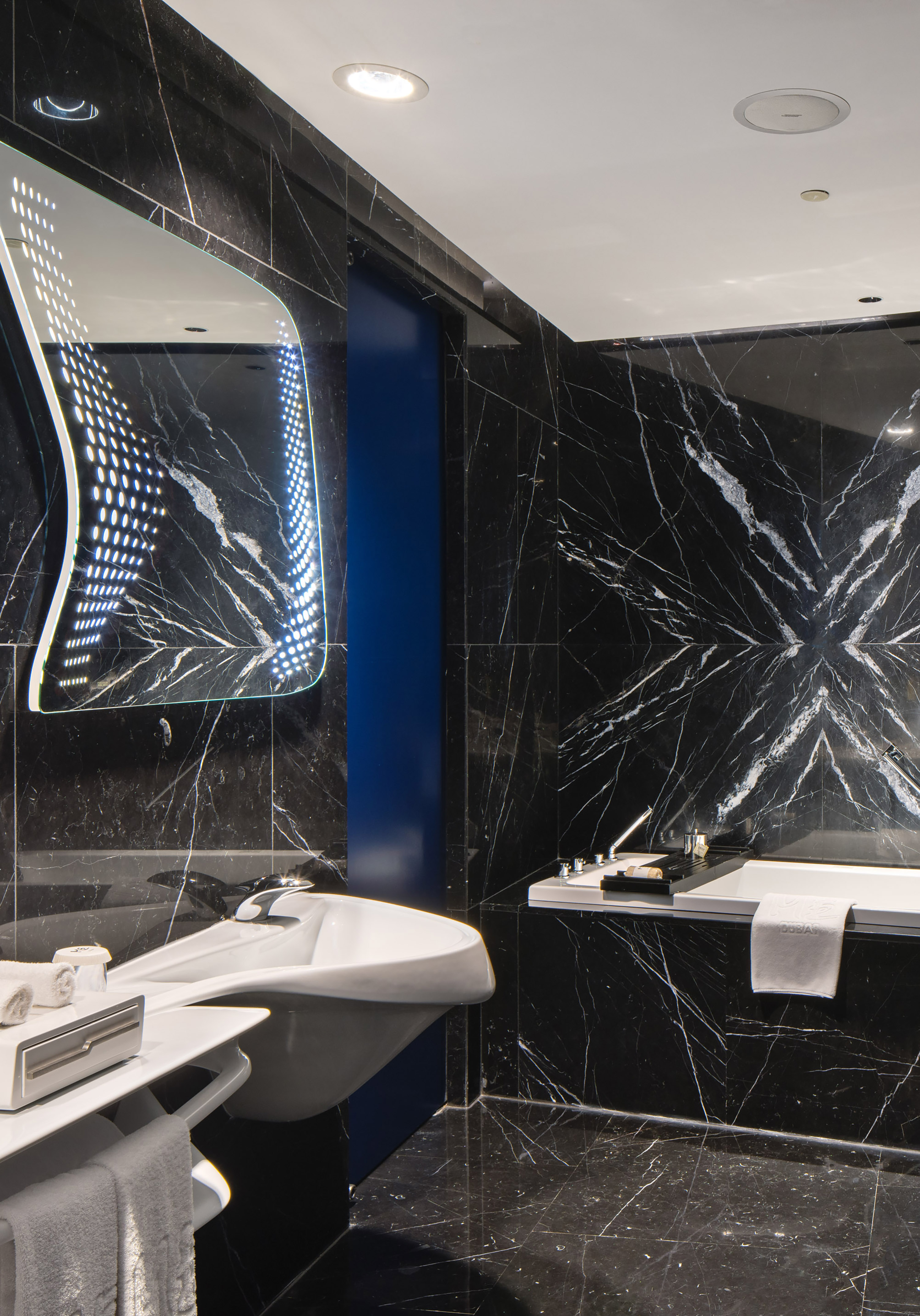 Black marble luxury bathroom with modern sink, illuminated mirror, and bathtub.
