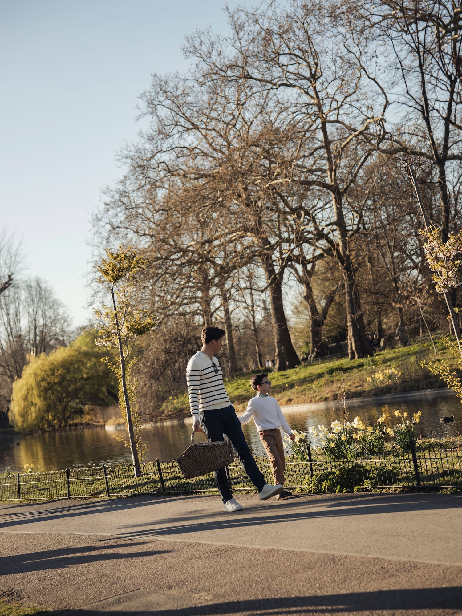 Father and son walking with picnic basket by a lake with daffodils in a park.