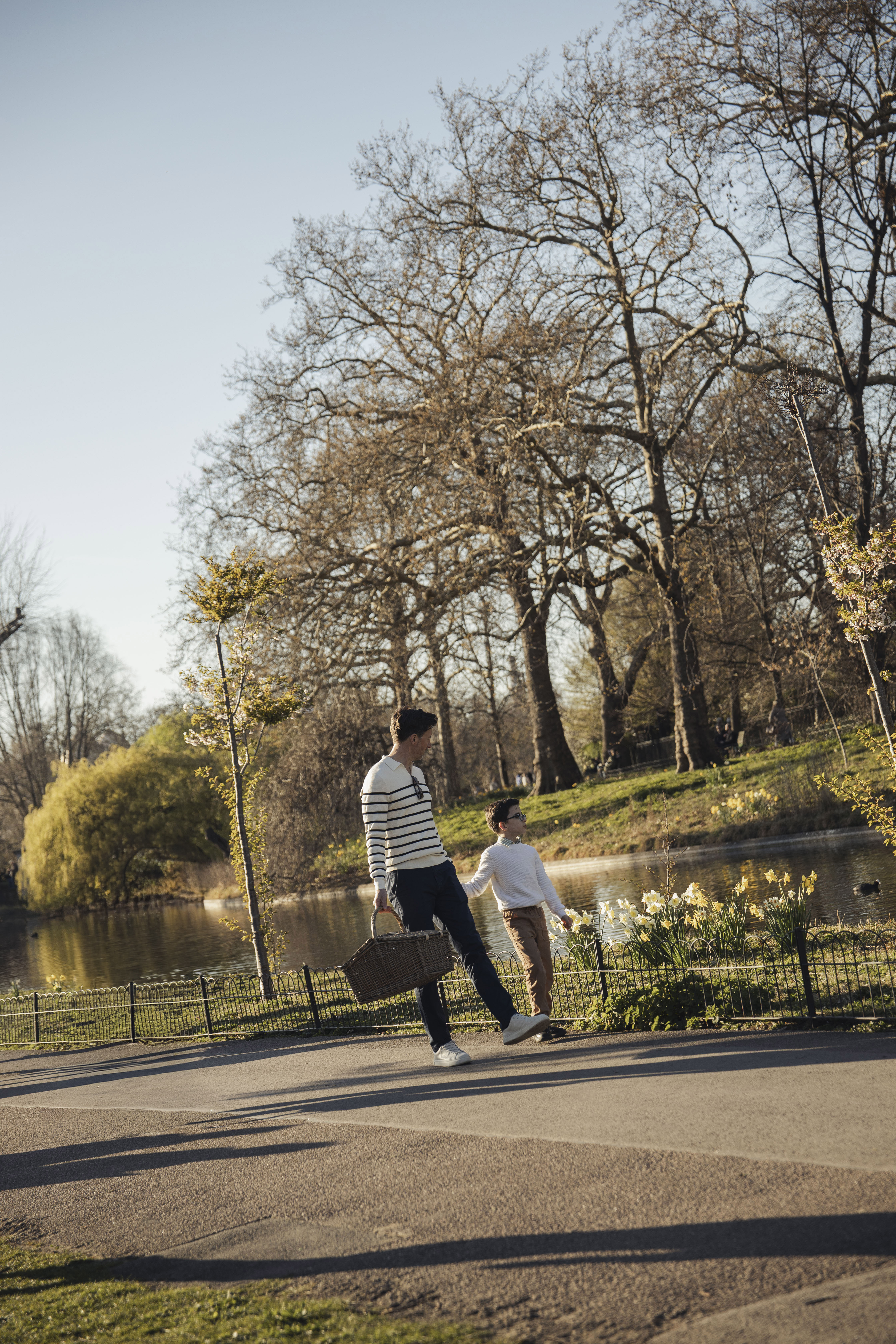 Father and son walking with picnic basket by a lake with daffodils in a park.