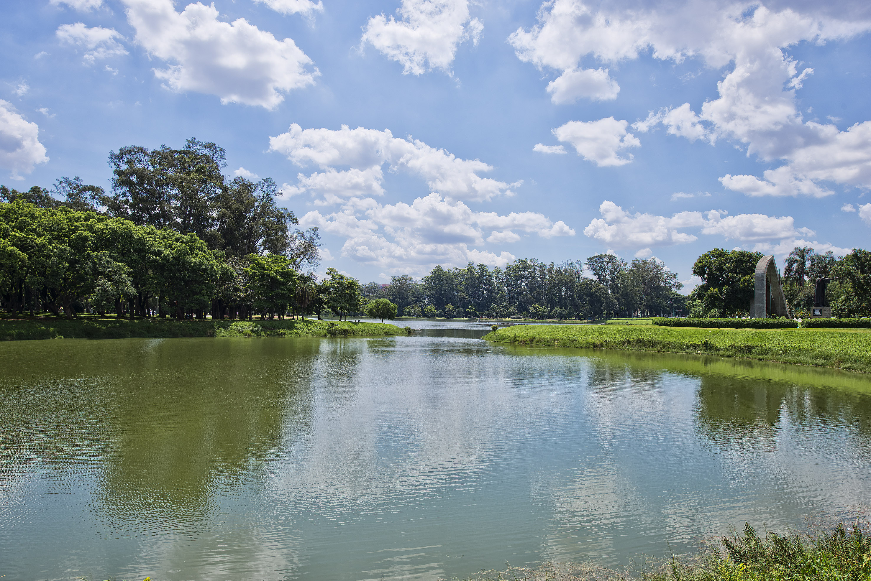 Ibirapuera Park lake, green trees, blue sky, white clouds.