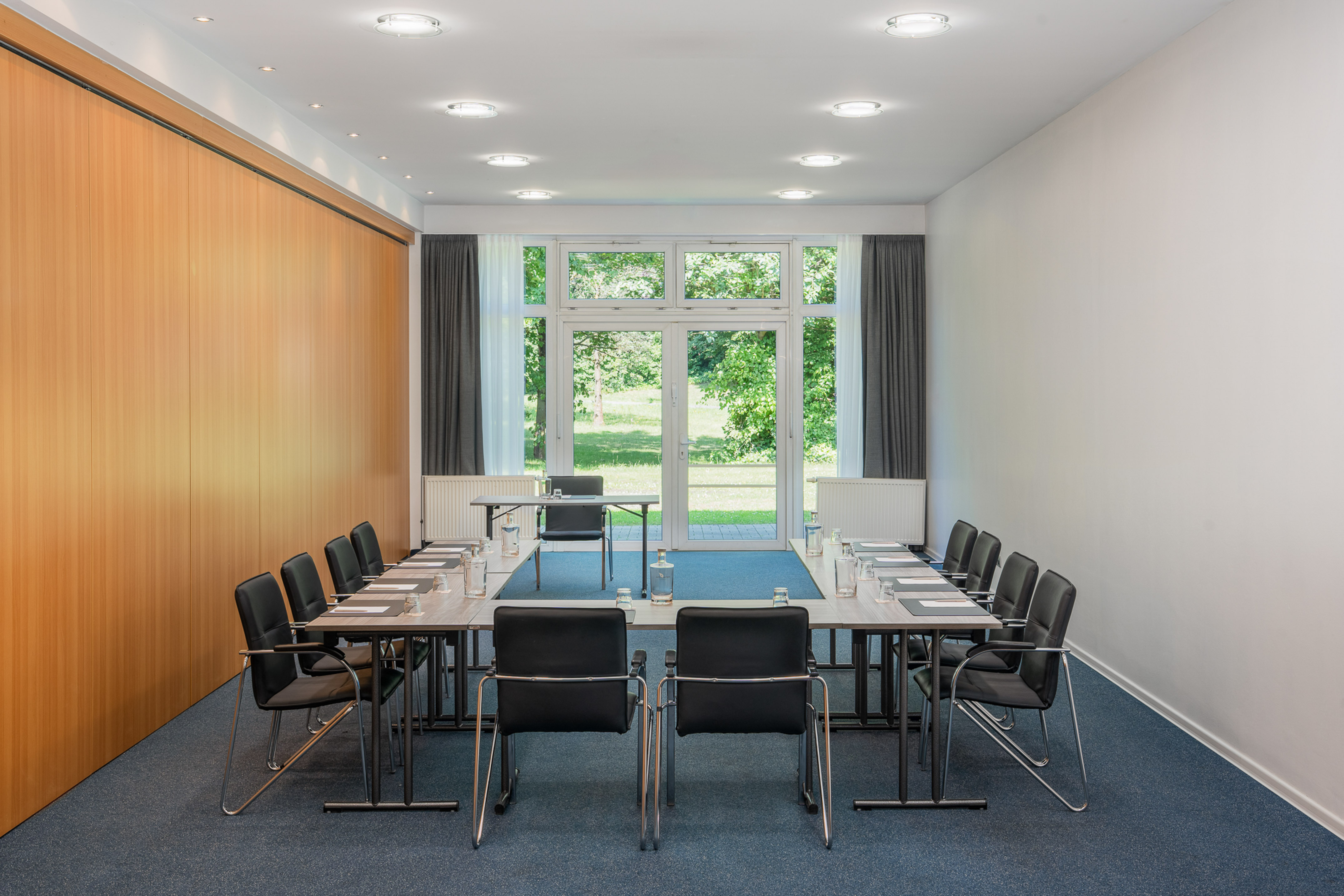 U-shaped meeting room with black chairs, wood paneling, and park view windows.