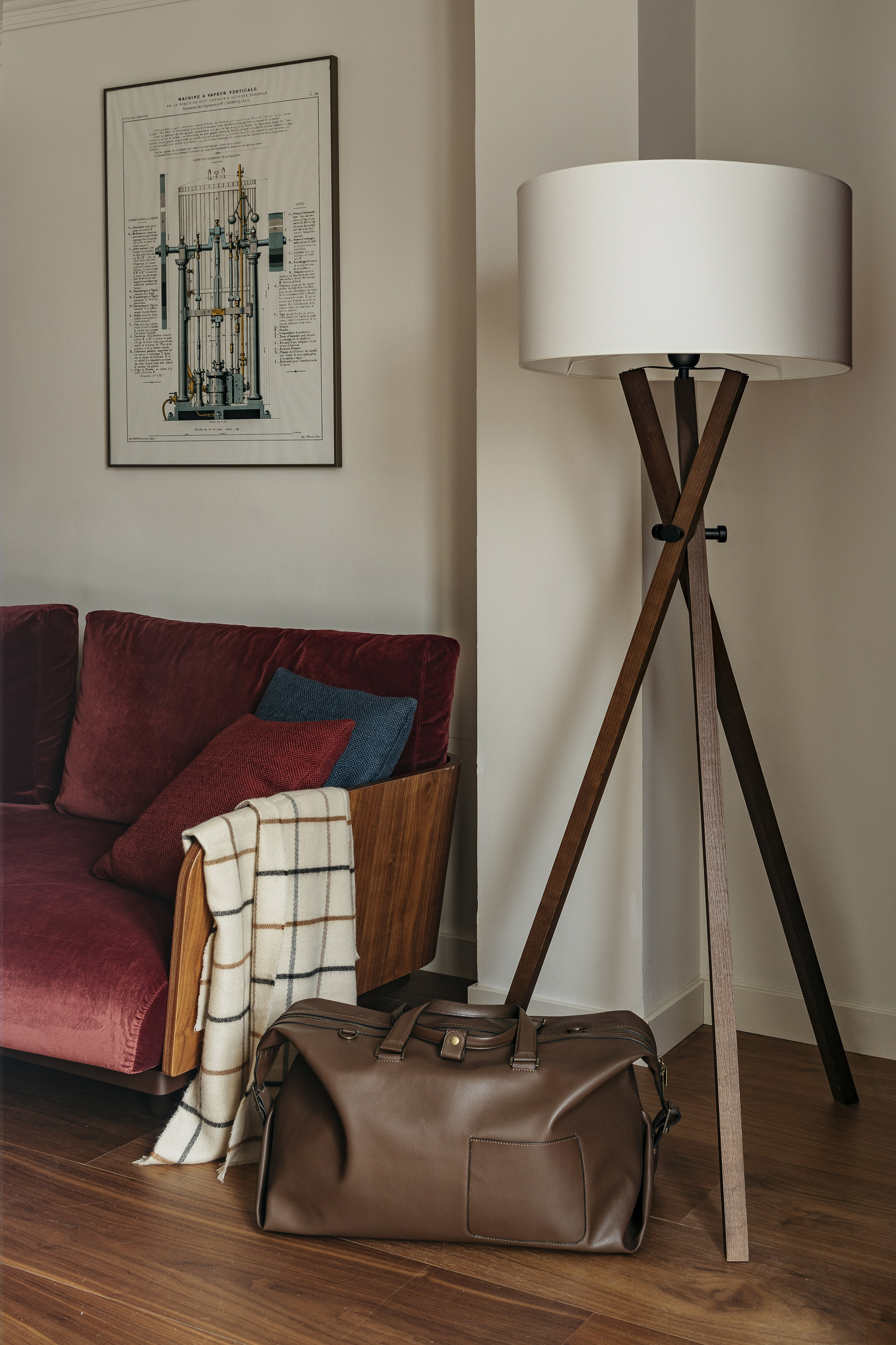 Red velvet sofa, wooden tripod lamp, brown duffel bag in modern living room.