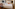 Modern hotel room with bed, diverse artworks, orange chair, and wall TV.