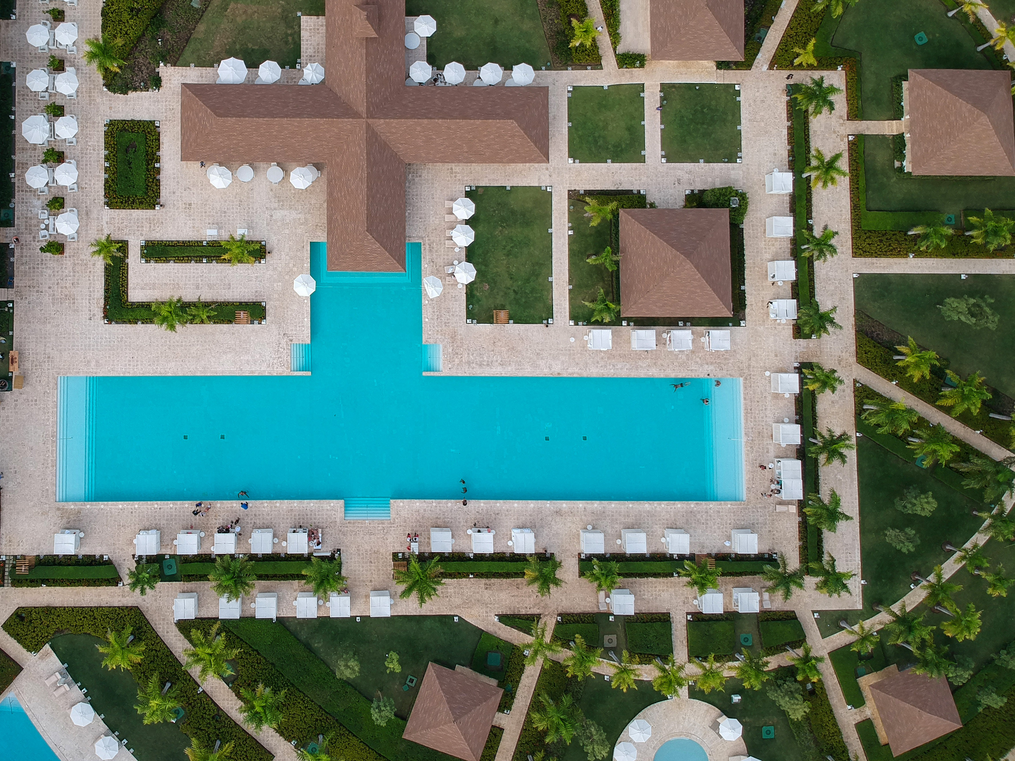 Aerial view: luxury tropical resort with blue pool, palm trees, brown buildings.