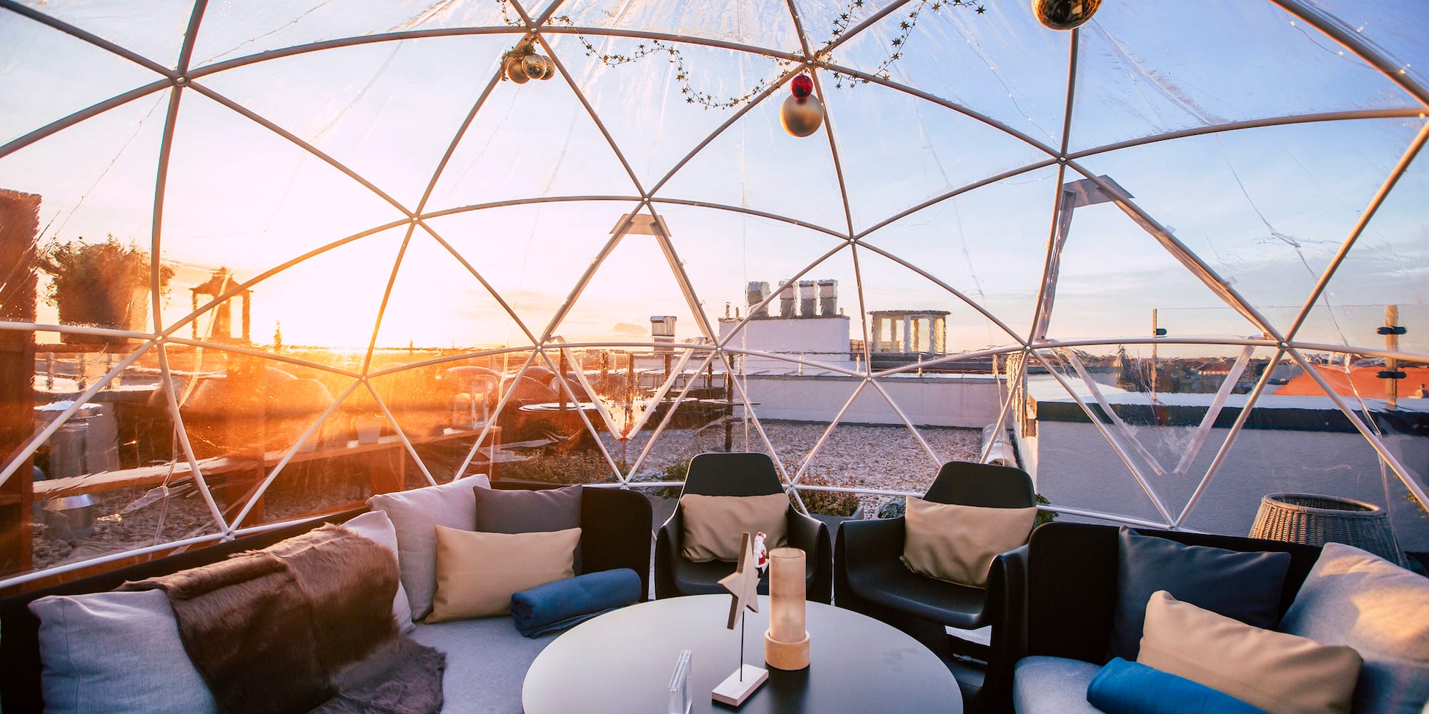 Rooftop igloo lounge with cozy seating, sunset city views, and festive decor.