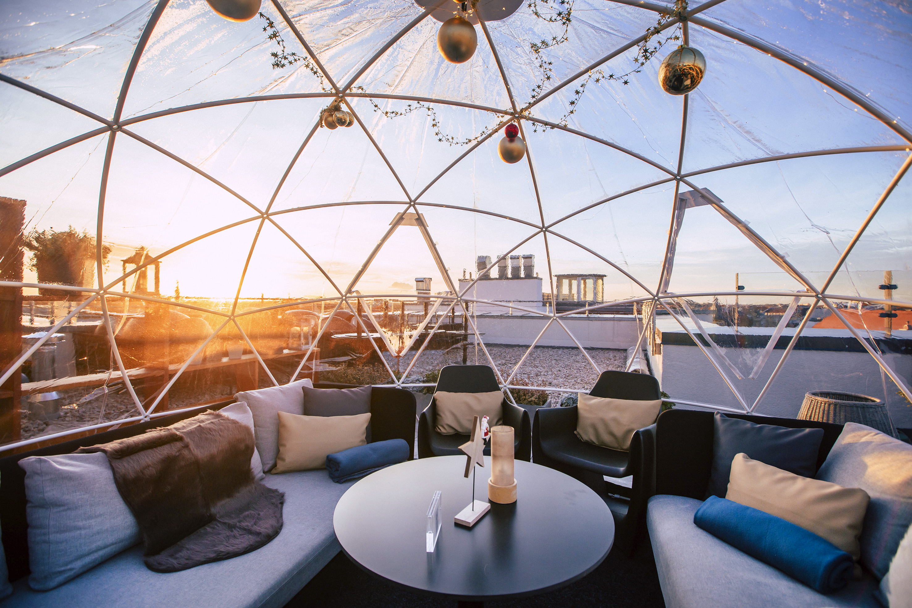Rooftop igloo lounge with cozy seating, sunset city views, and festive decor.