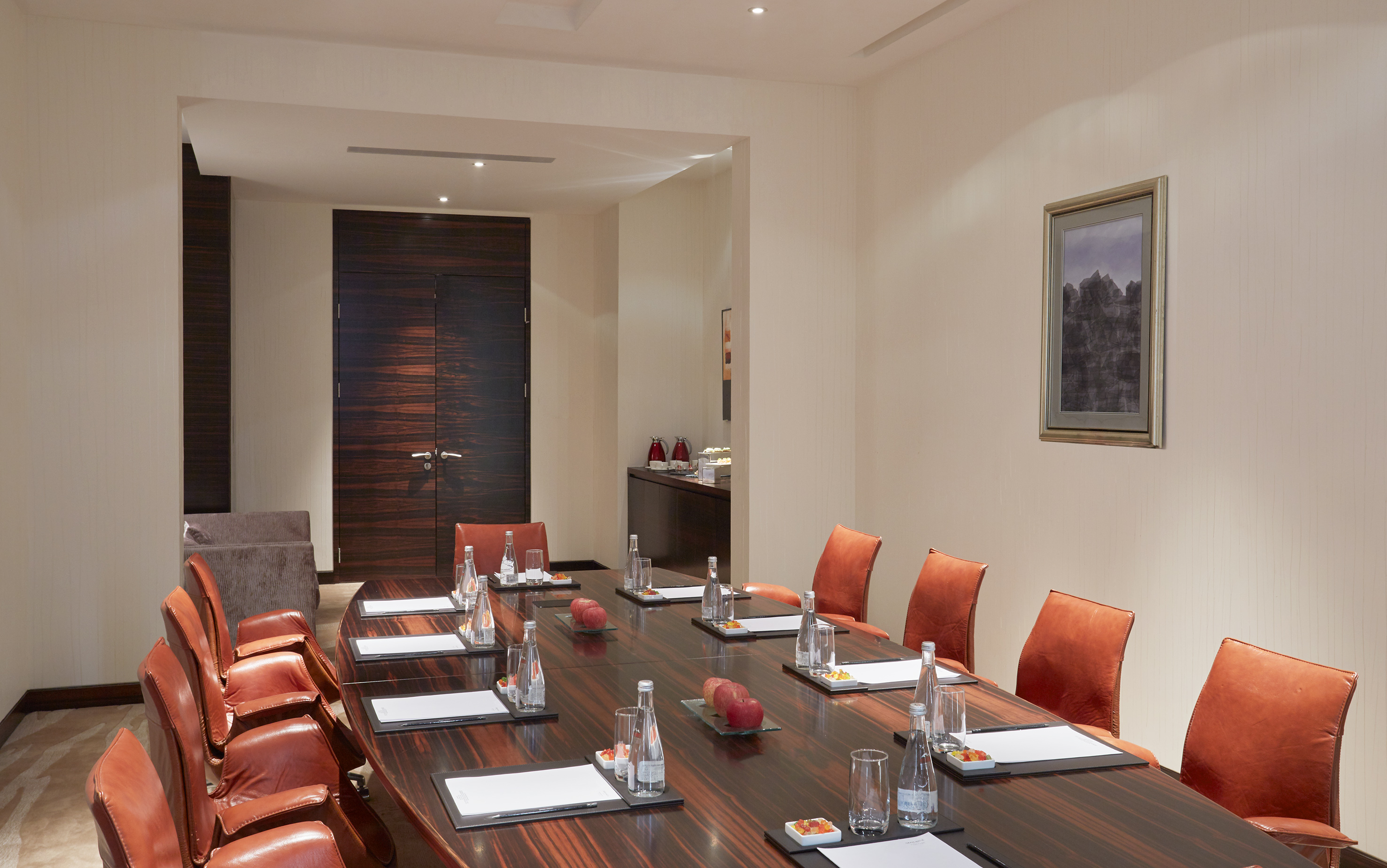 Modern conference room with dark wooden table, orange chairs, and water bottles.