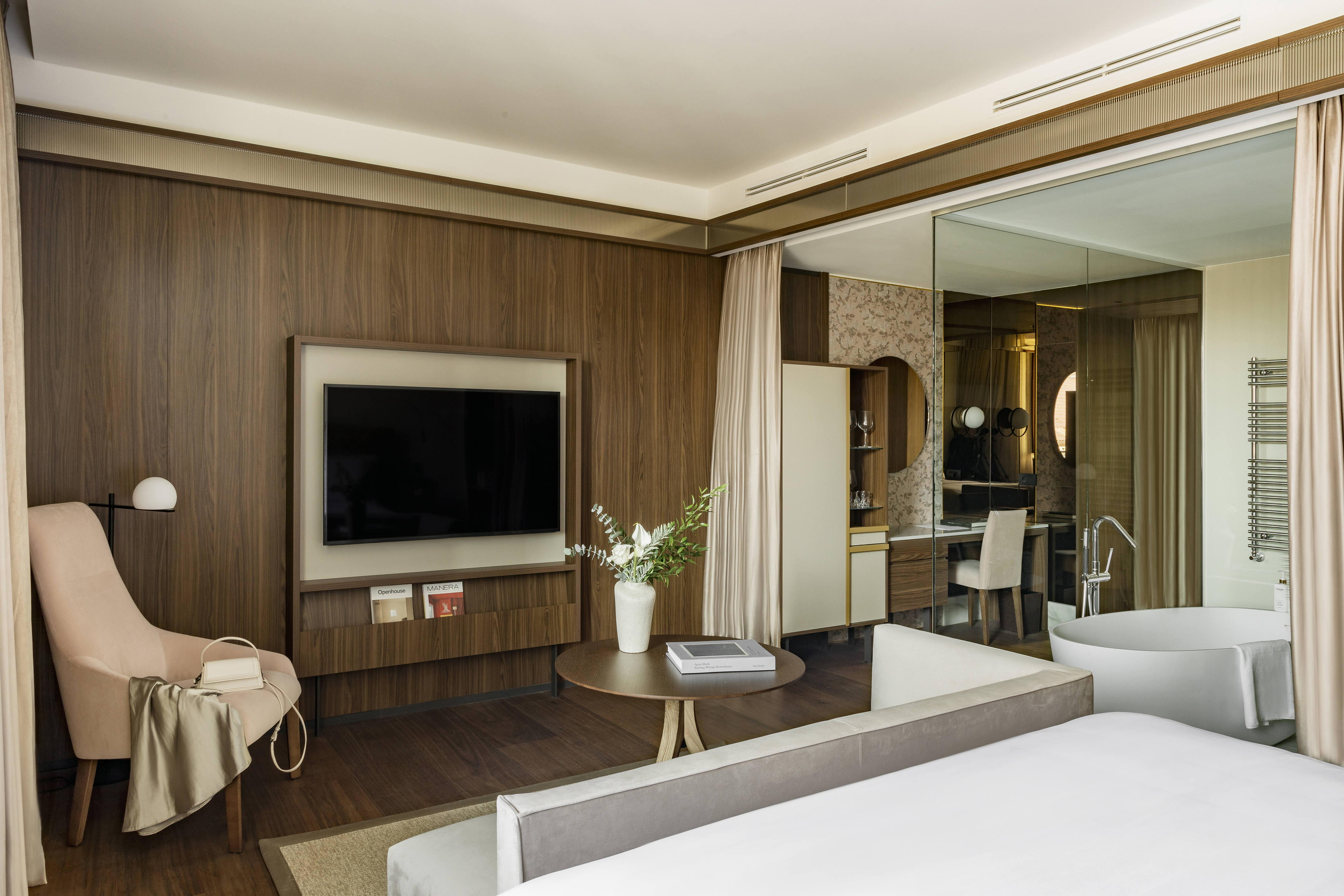 Luxurious modern hotel room with wood accent wall, TV, and freestanding tub.