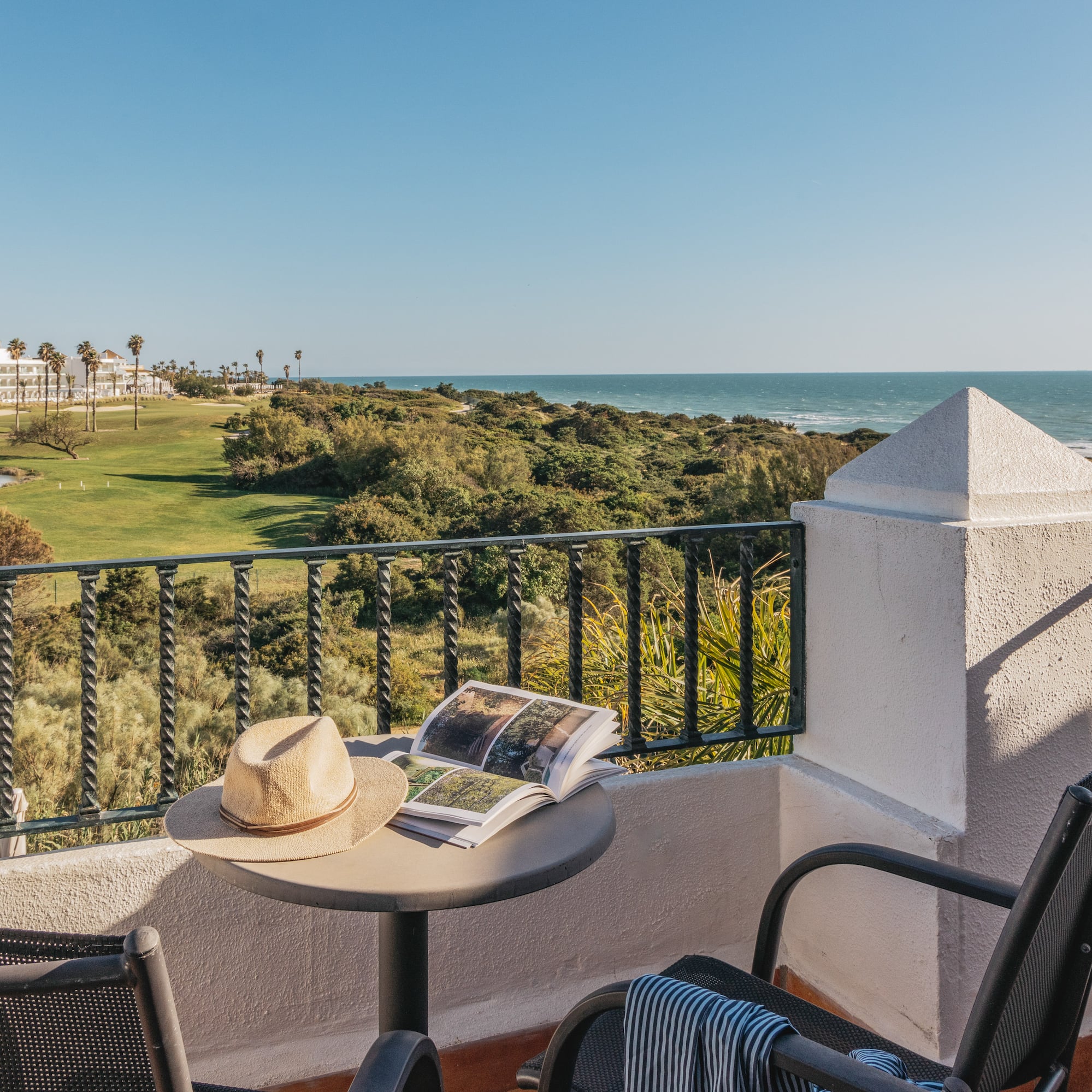 Resort balcony overlooking ocean and golf course with hat and book.