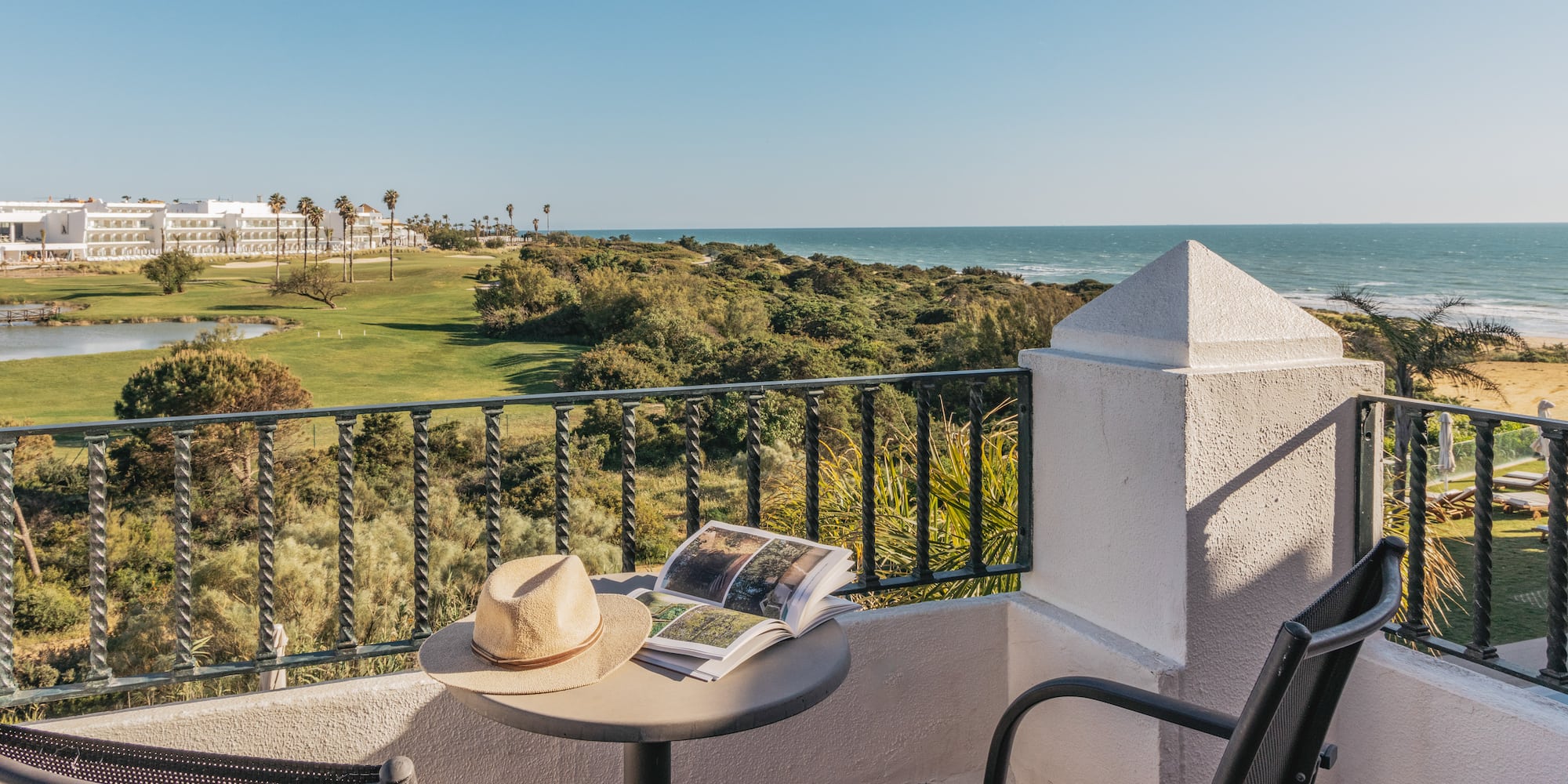 Resort balcony overlooking ocean and golf course with hat and book.