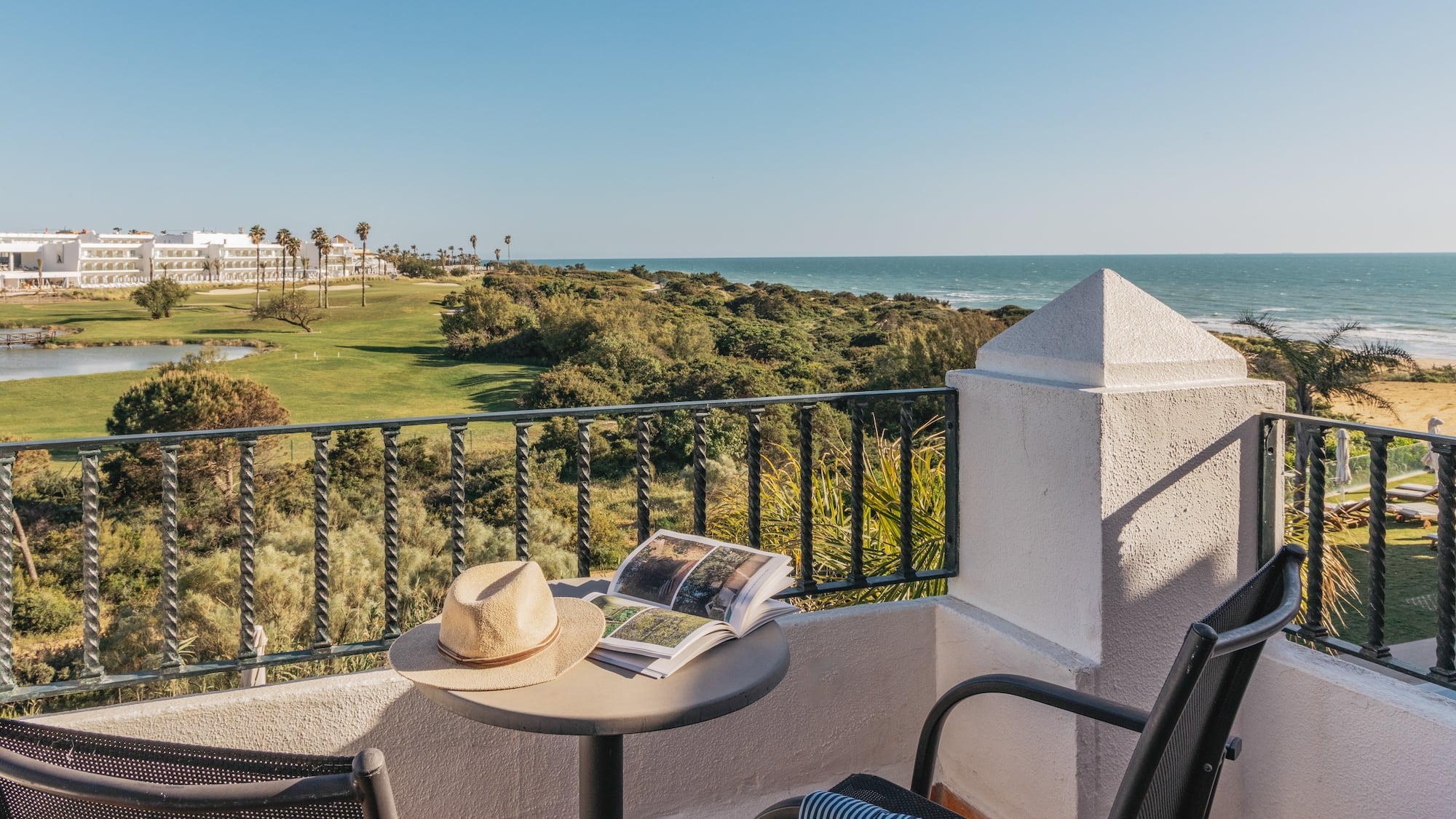 Resort balcony overlooking ocean and golf course with hat and book.
