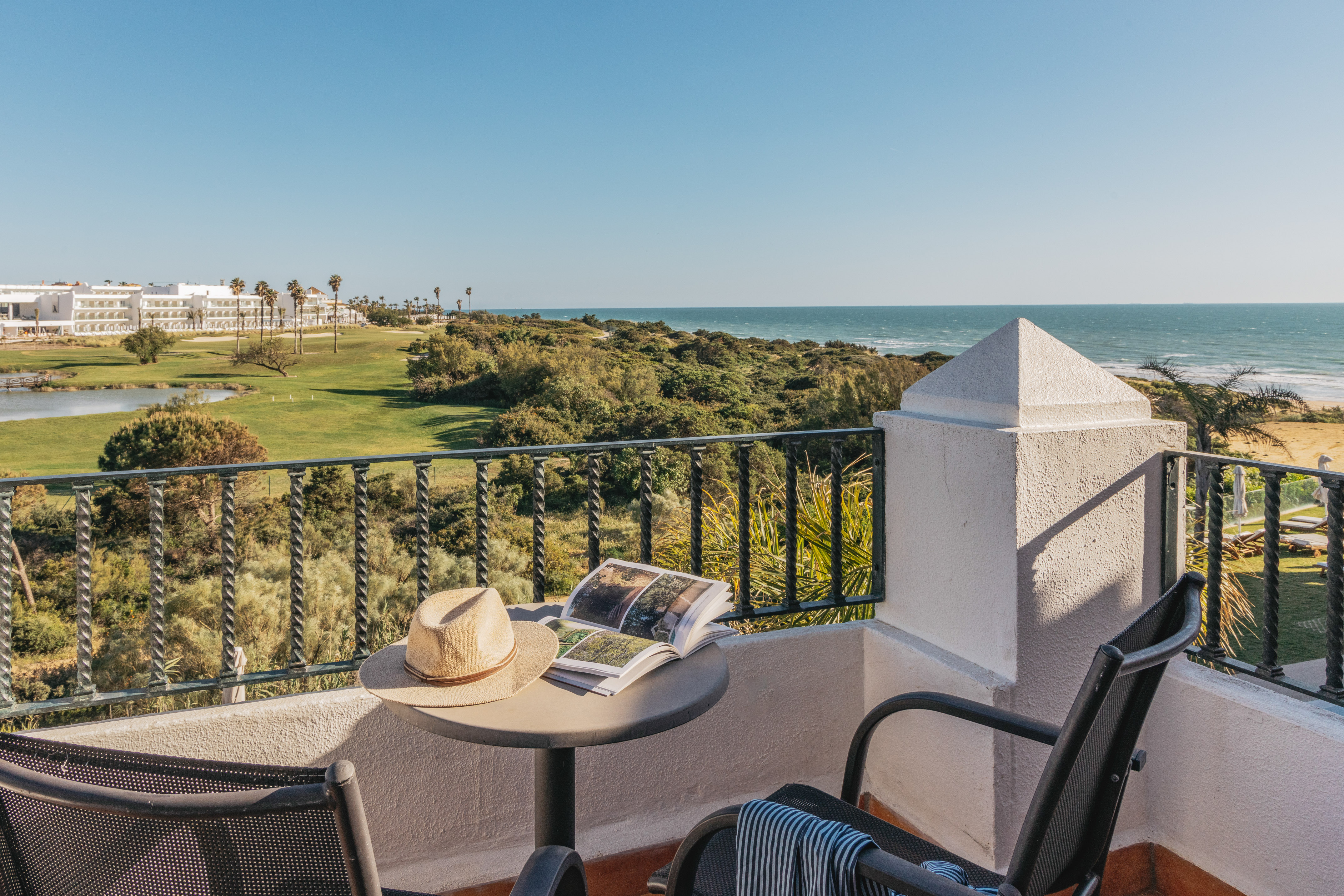 Resort balcony overlooking ocean and golf course with hat and book.