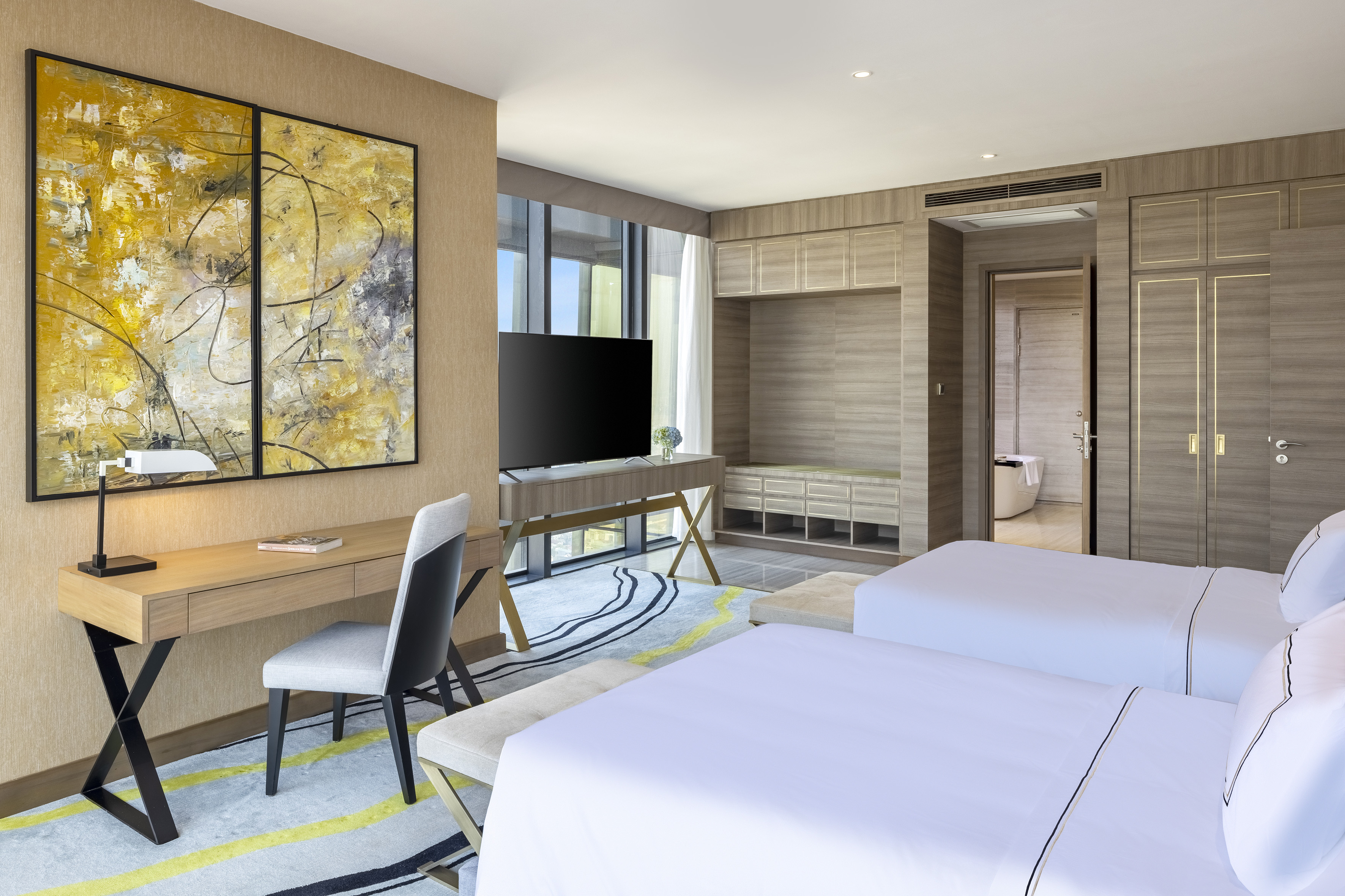 Stylish hotel bedroom with twin beds, modern desk, TV, and abstract art.