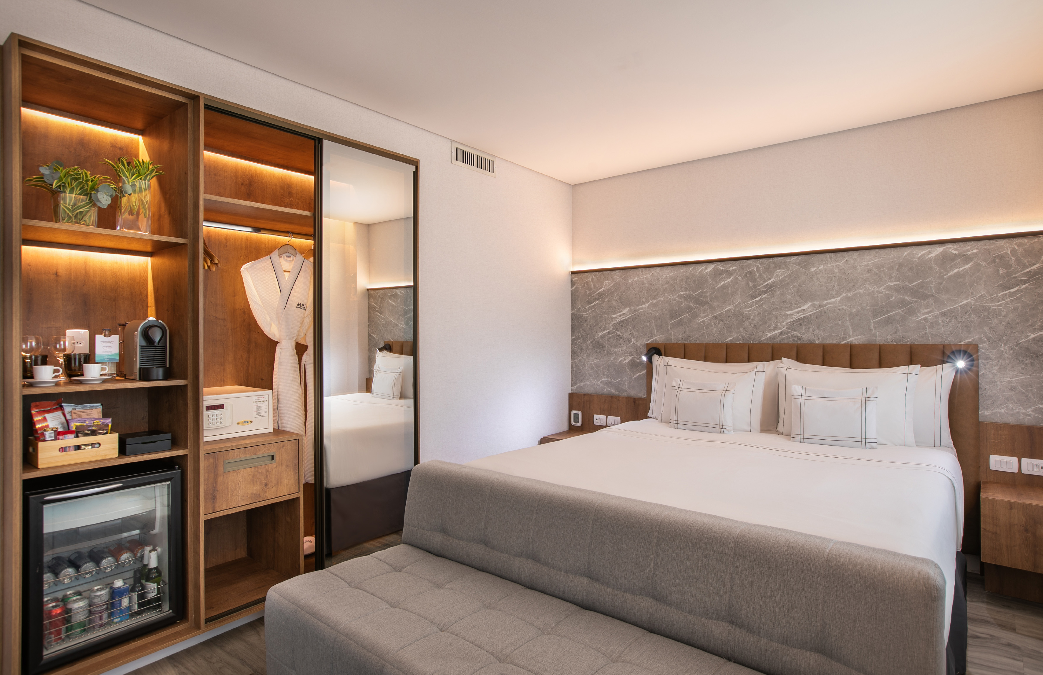 Modern hotel room: bed, marble wall, built-in wardrobe, Nespresso, and mini-bar.
