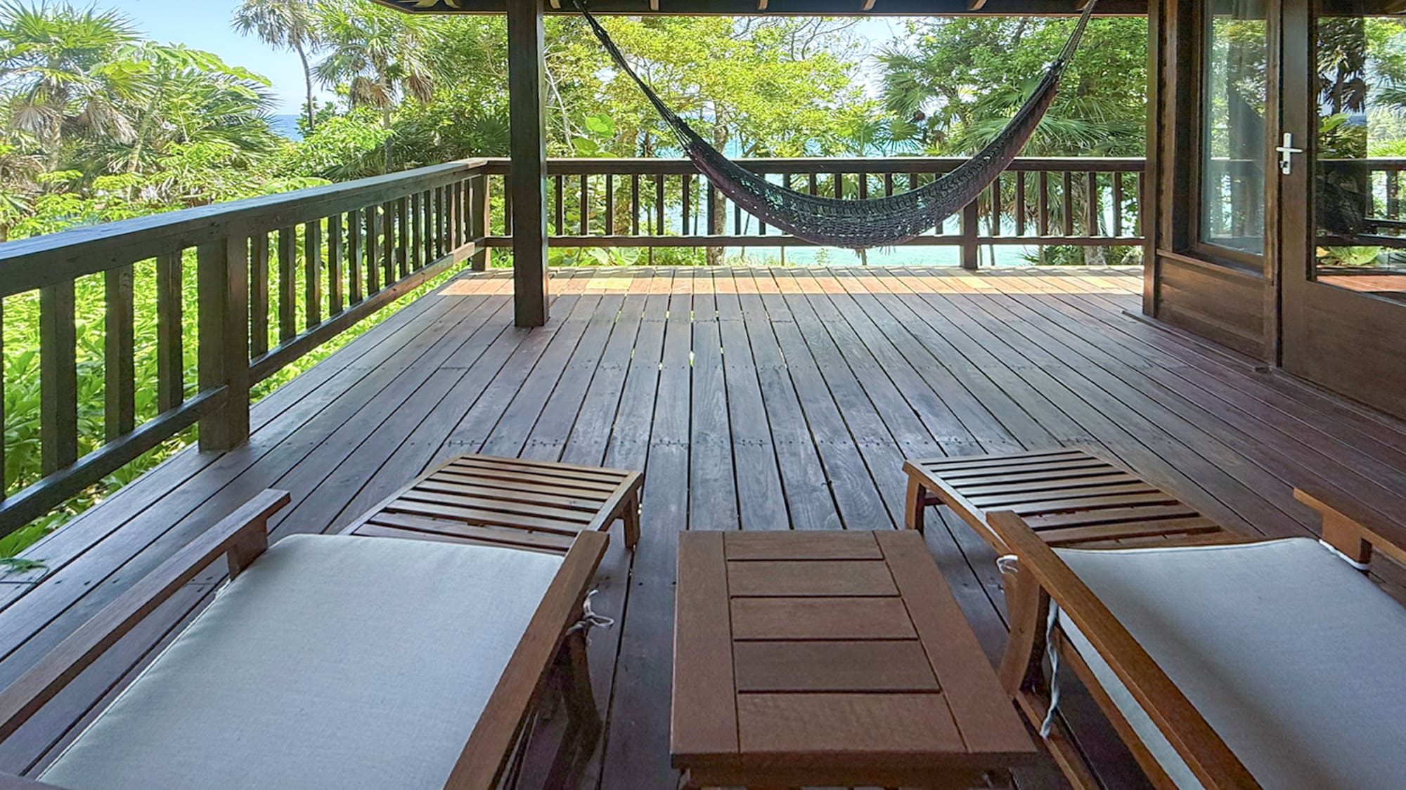 Tropical wooden deck with hammock, lounge chairs, and ocean view.
