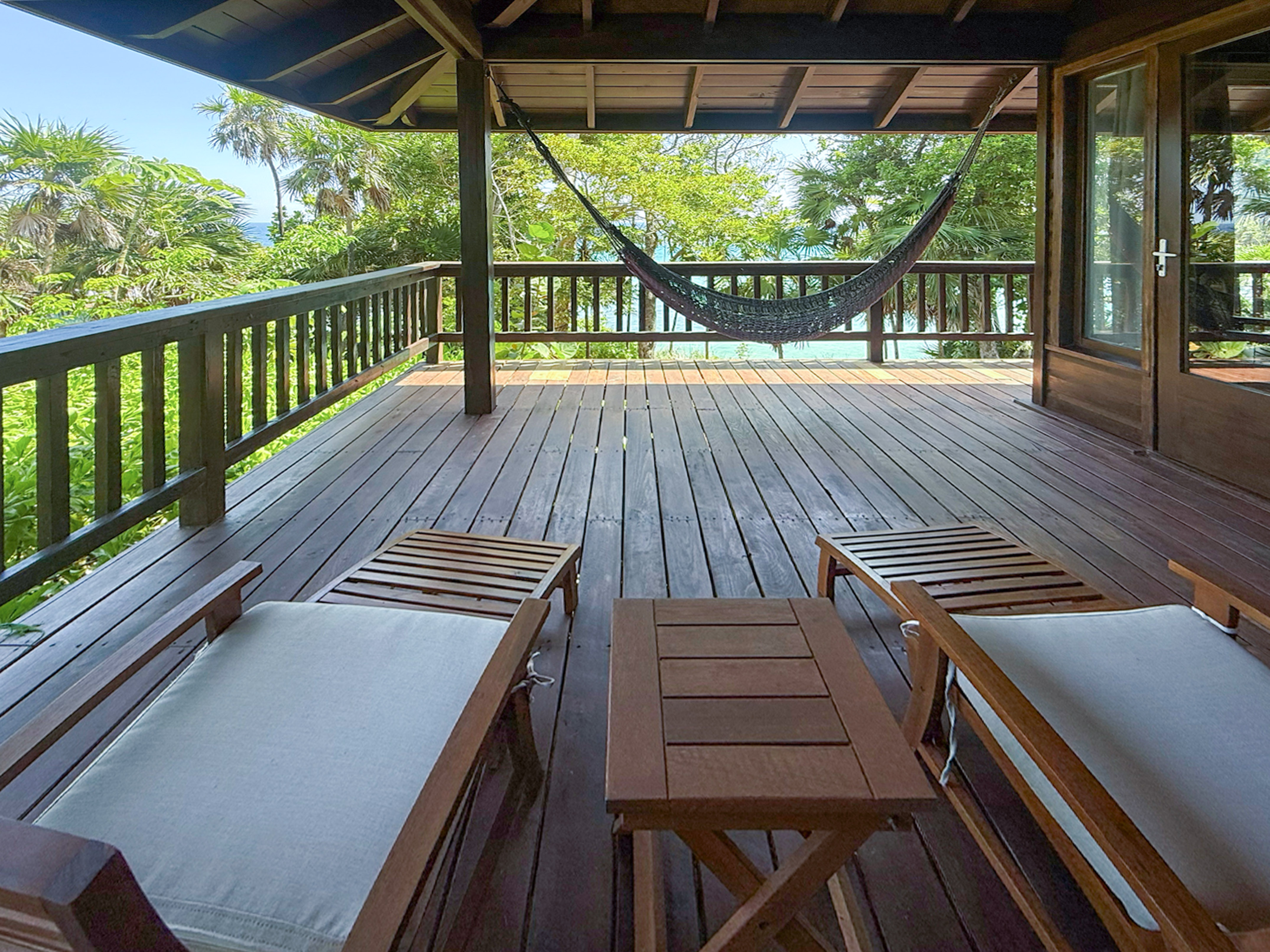 Tropical wooden deck with hammock, lounge chairs, and ocean view.