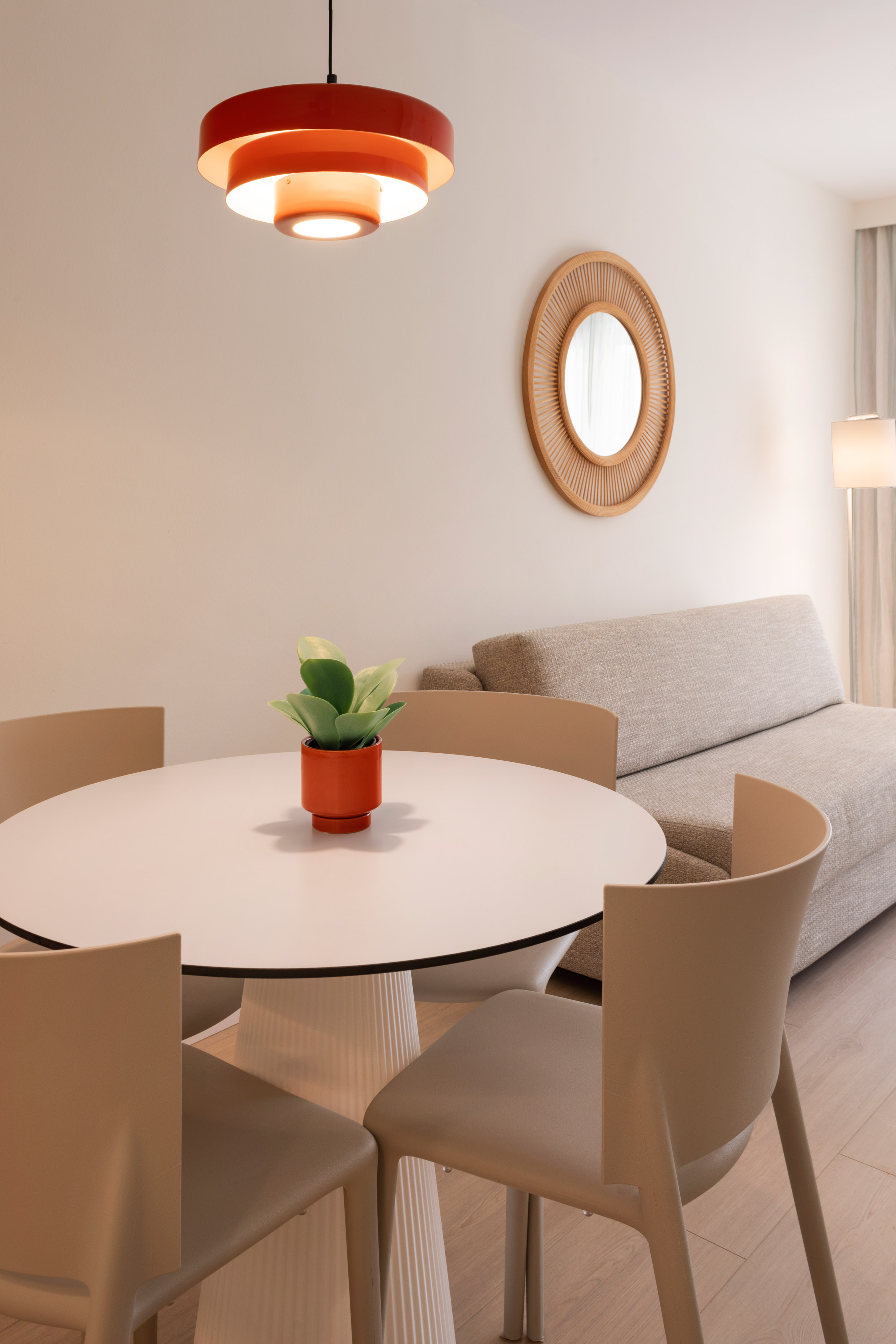 Modern dining area with round table, chairs, orange pendant, and sofa.